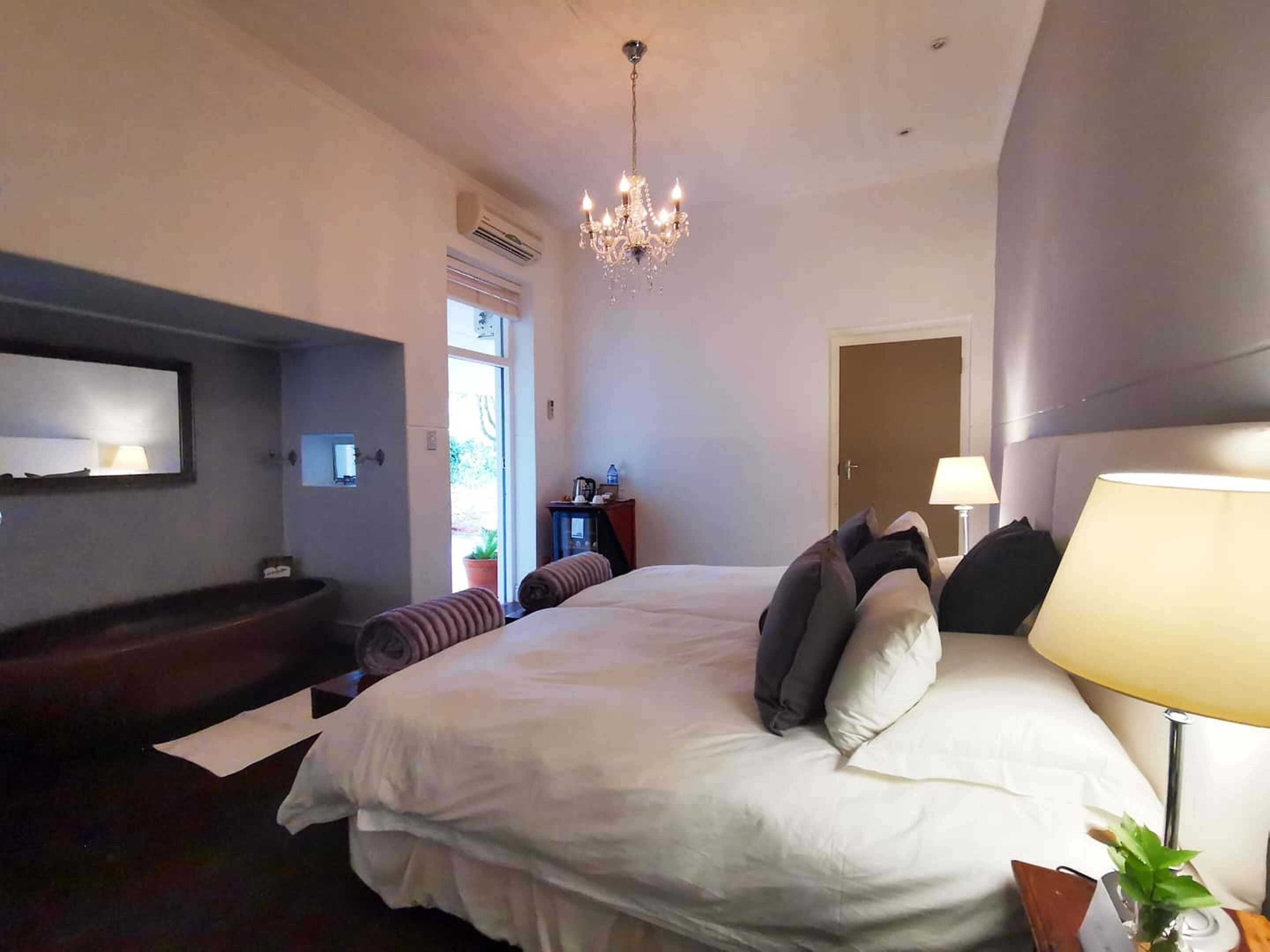 Un dormitorio moderno con una cama grande, una mesita de noche con lámpara, un televisor en la pared y una araña.
