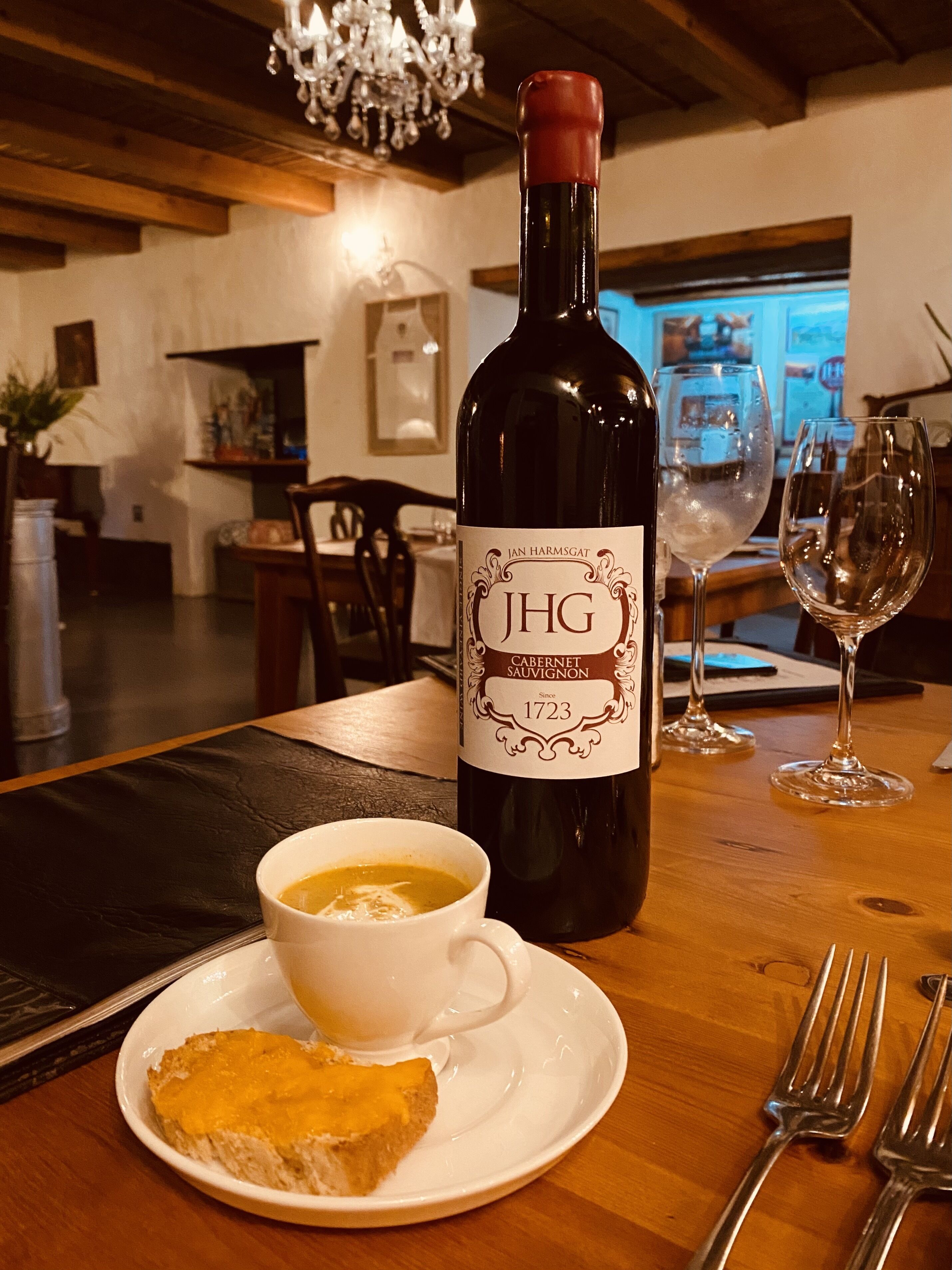 A bottle of JHG Cabernet Sauvignon on a table with a cup of tea and a slice of cake.