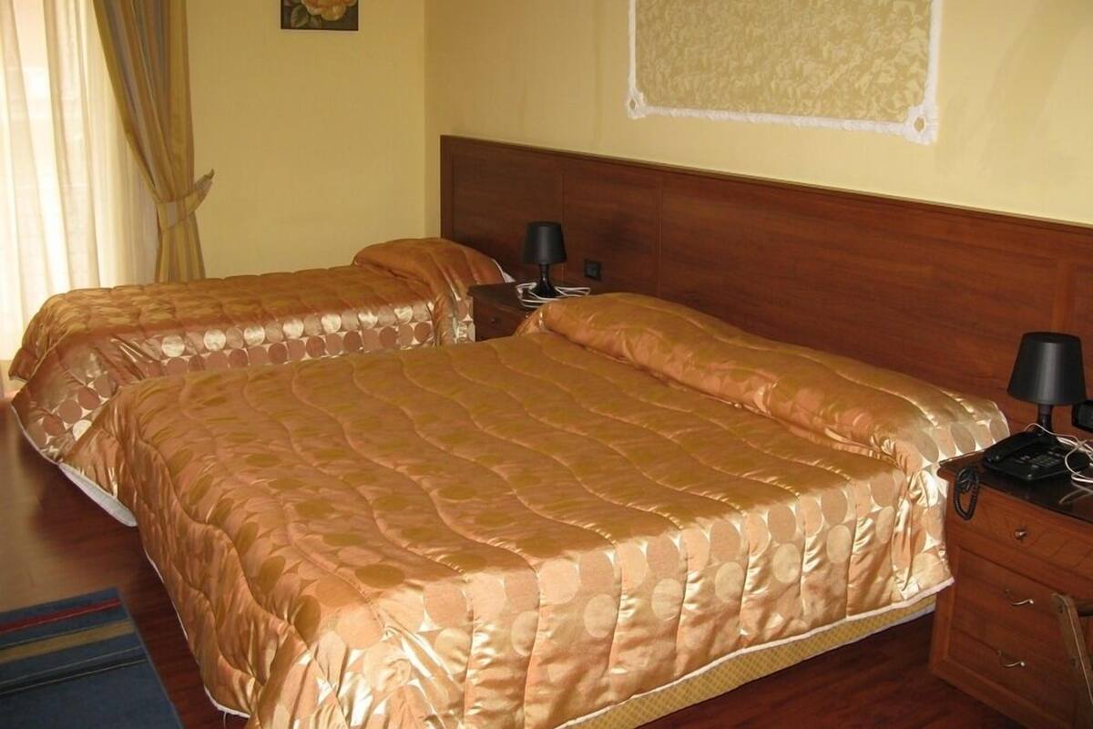 Ein Doppelbett mit Holz-Kopfteil, ein Nachttisch mit Lampe und ein an der Wand befestigtes Korkbrett.