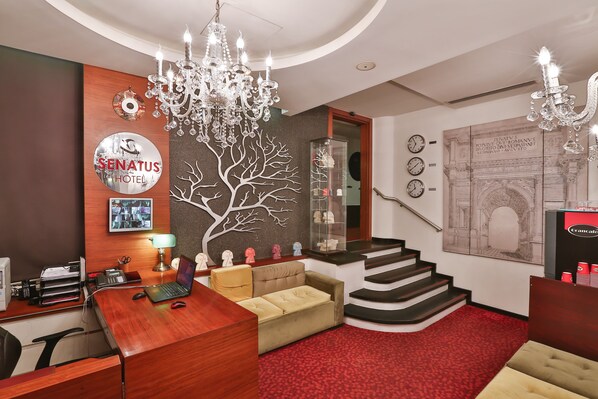 A hotel lobby with a wooden reception desk, a sofa, a chandelier, and a staircase. - Senatus Hotel - Special Class (Istanbul)