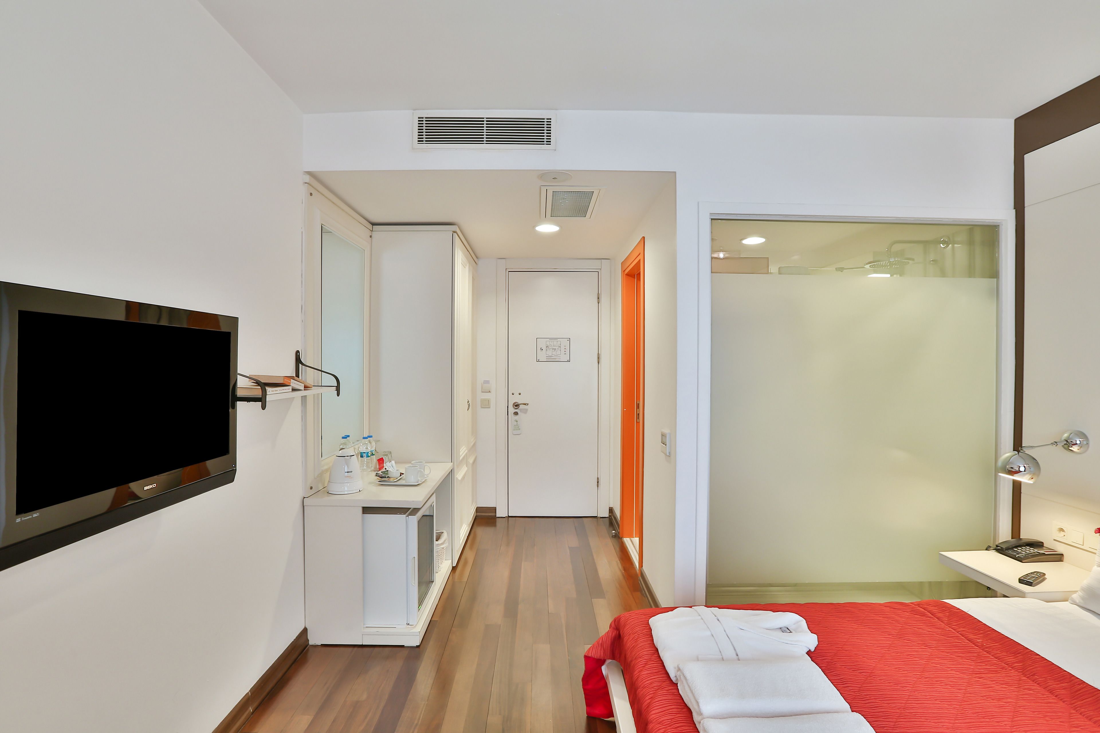 A hotel room with a bed, a TV, a desk with a chair, and a bathroom with a shower.