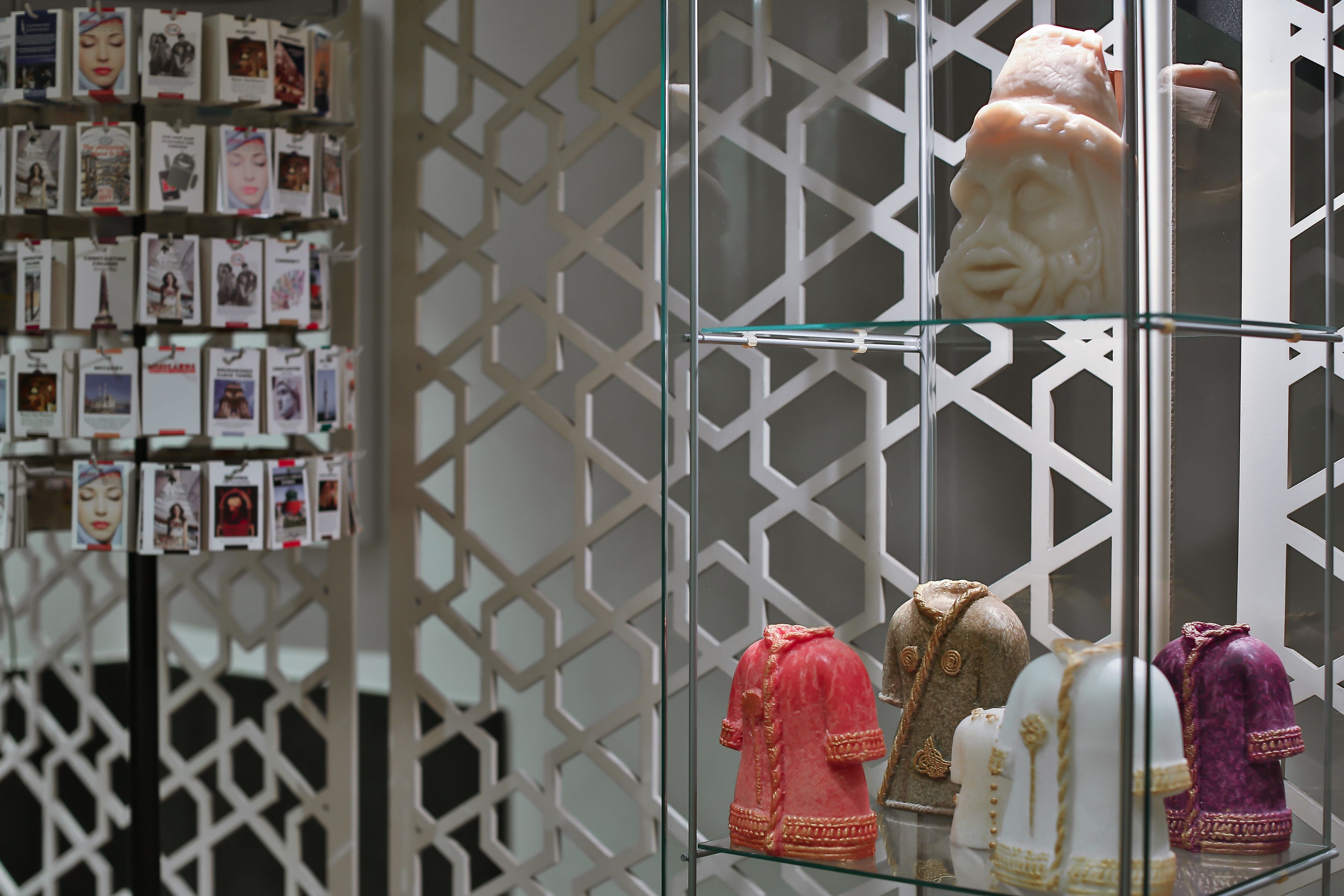 A display of traditional headgear on glass shelves against a geometric patterned wall.