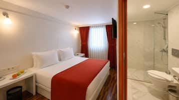 A hotel room with a bed, bedside table, and a shower area.