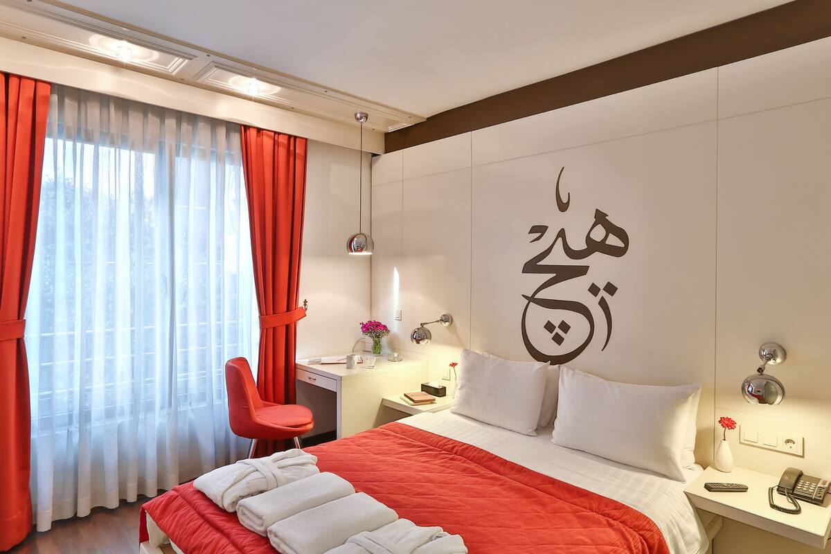A hotel room with a bed, a desk, a chair, and a large wall decoration.