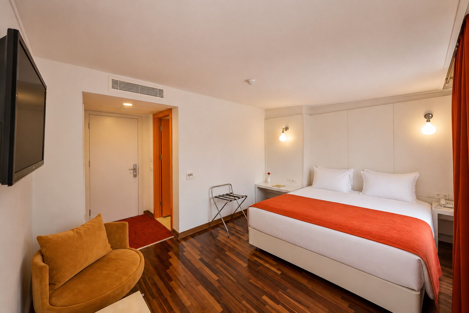 A hotel room with a bed, a chair, a desk, a TV, and a door.