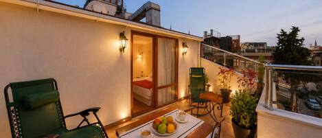 Un balcon avec une table dressée pour deux personnes, des chaises, un pot de fleurs et une vue sur le paysage urbain.
