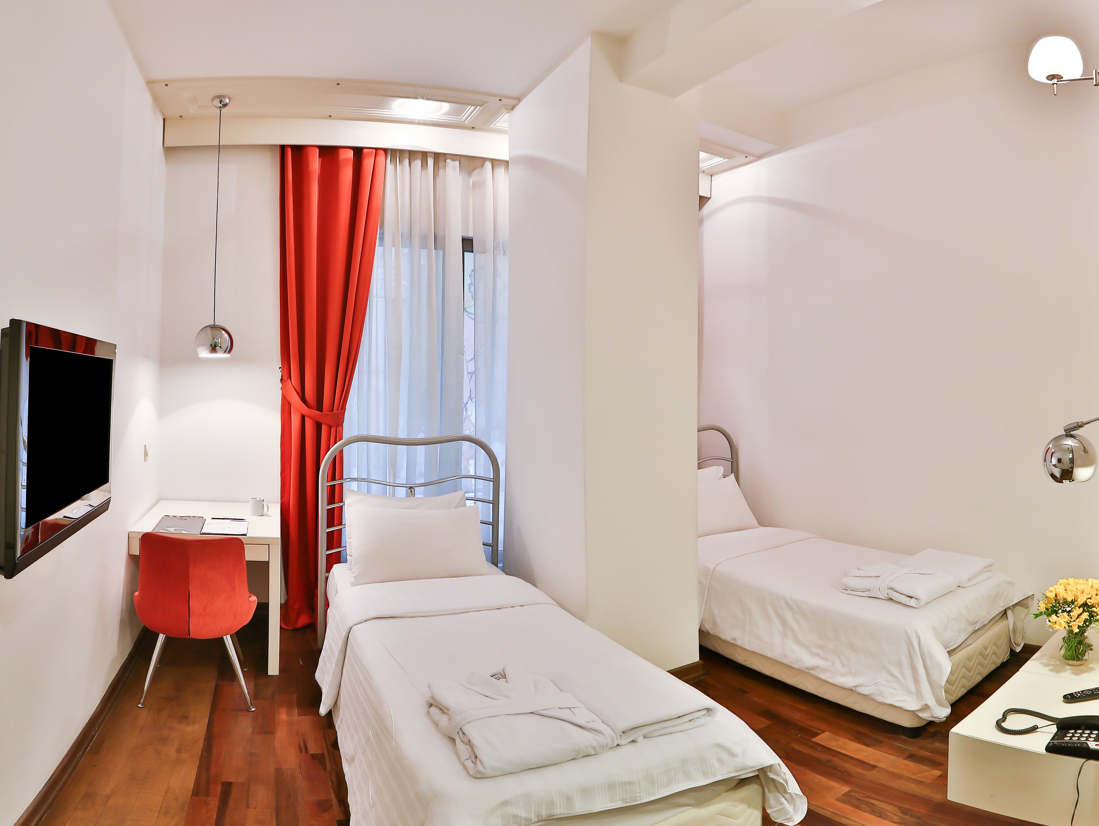 Quarto de hotel com cama, escrivaninha, cadeira, televisão e janela com cortinas.