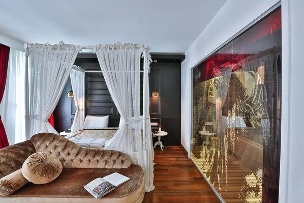 Een slaapkamer met een hemelbed, een zithoek met een comfortabele bank, en een groot raam met uitzicht op een stadsgezicht.