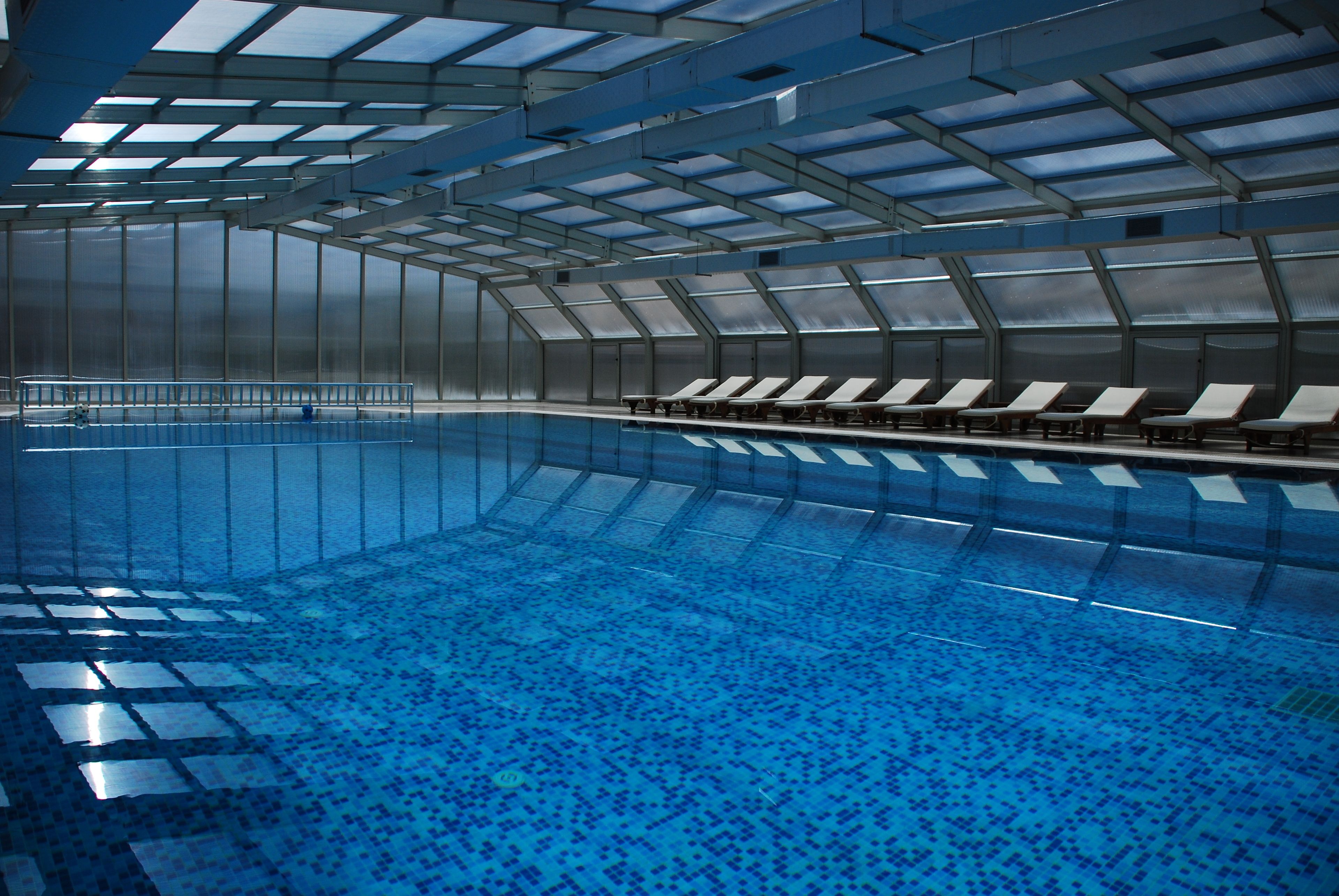 An indoor swimming pool with a tiled floor and a row of sun loungers along the side.