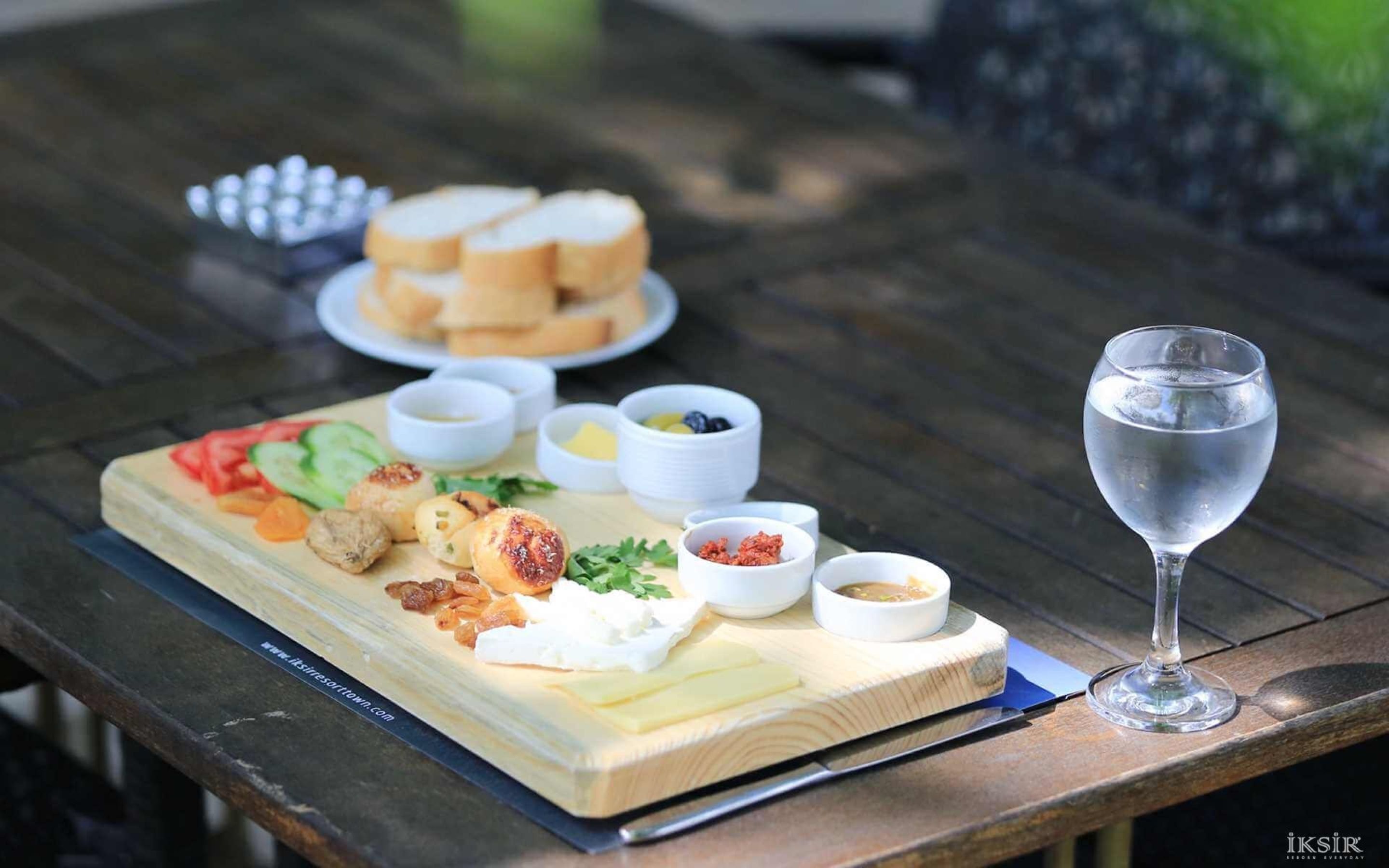 A wooden table with a charcuterie board, a glass of water, and a plate of bread.