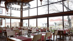 Een restaurant met meerdere tafels en stoelen, grote ramen en een hanglamp.
