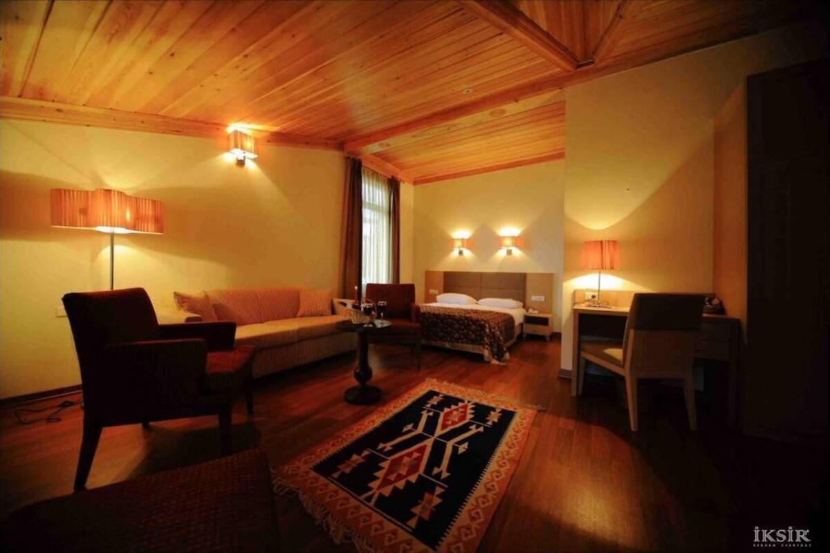 A cozy room with a wooden ceiling, a sofa, a bed, a desk, and two wall-mounted lamps.