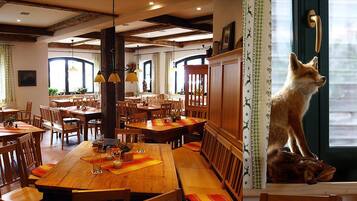 Ein Restaurant mit Holztischen und -stühlen, einem Fuchs an der Tür und großen Fenstern.