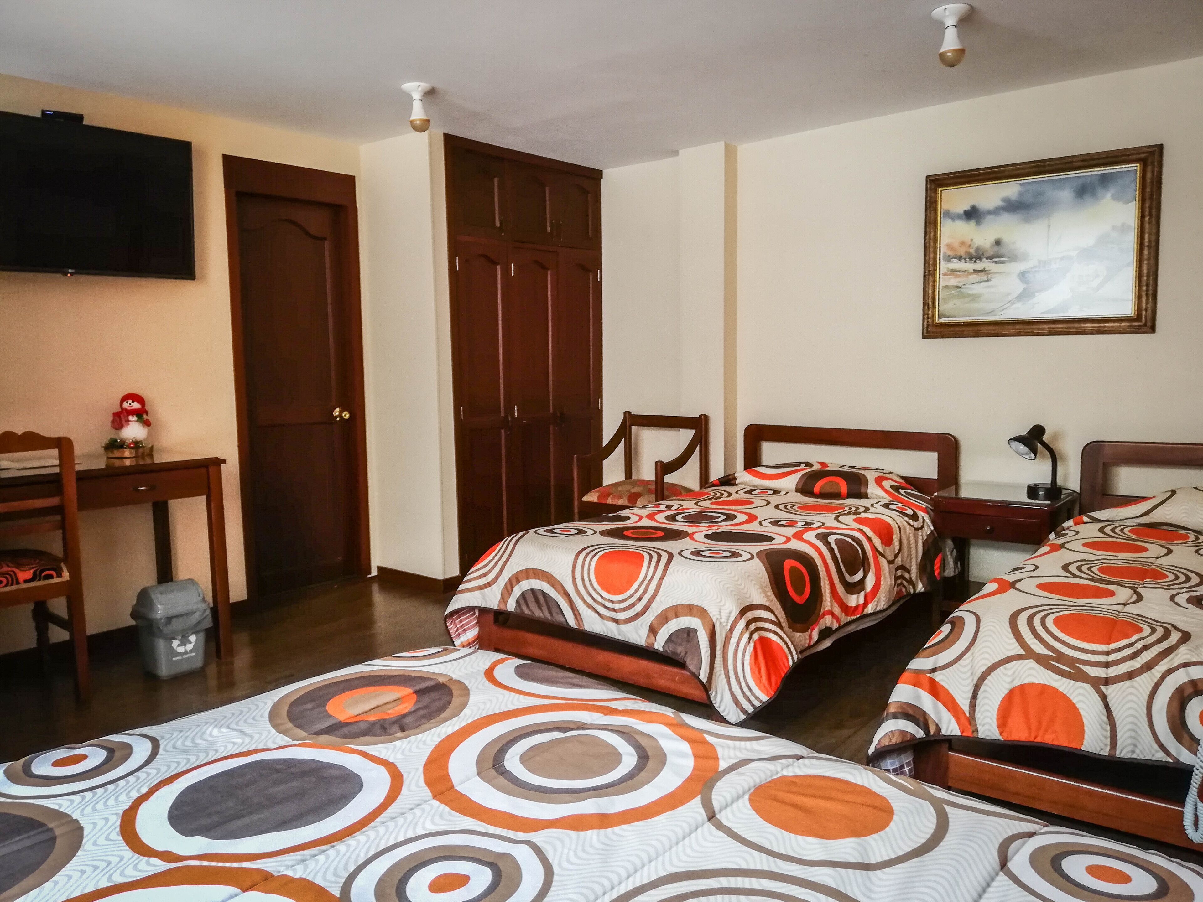 A hotel room with two beds, a desk, a chair, a television, and a painting on the wall.