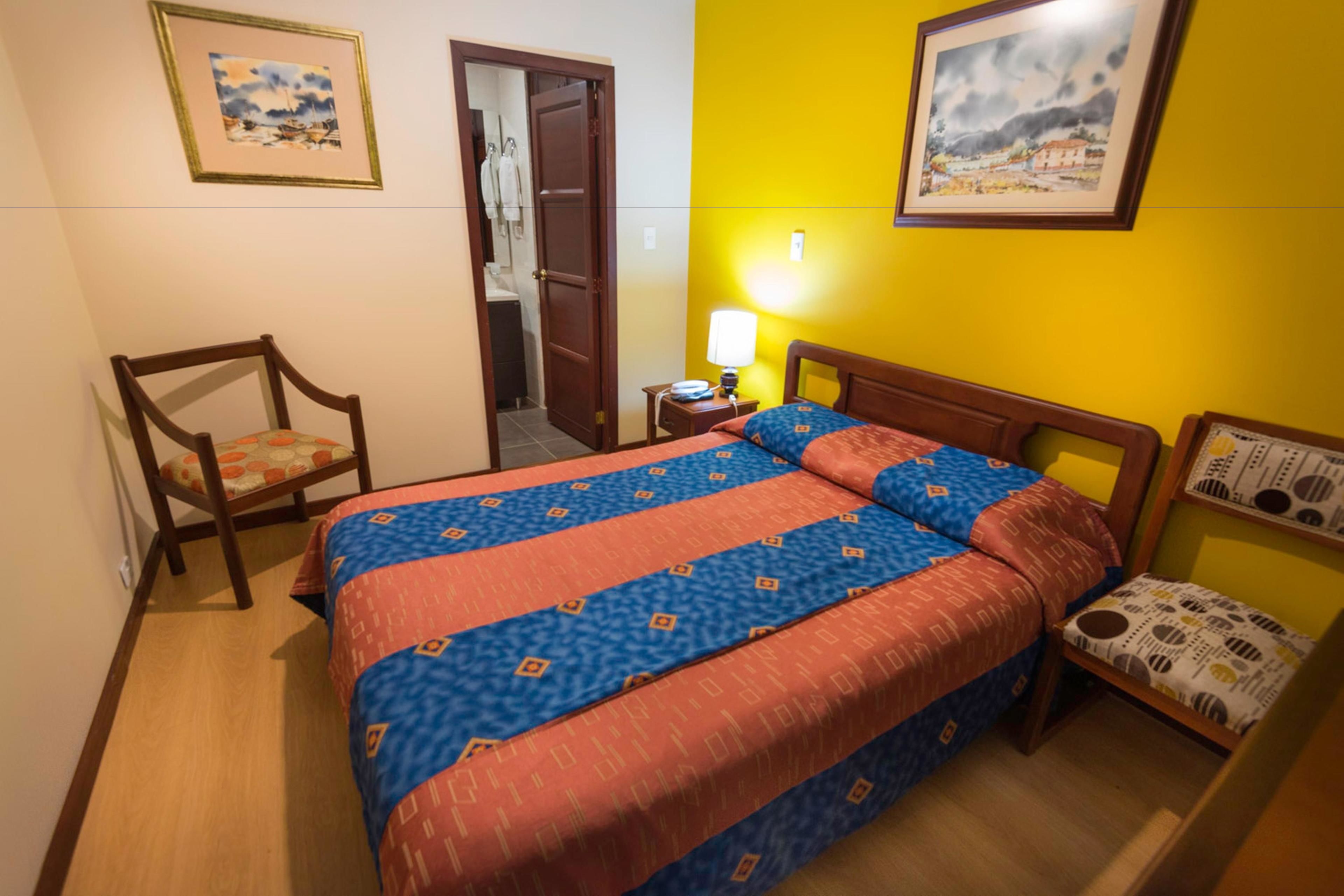 A hotel room with a bed, a chair, a nightstand, and a wall with two framed pictures.
