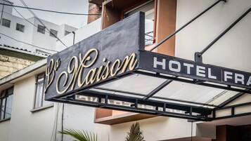 Un cartel de hotel con el nombre 'Maison Hotel' en una tipografía clásica, sujeto a una estructura metálica.