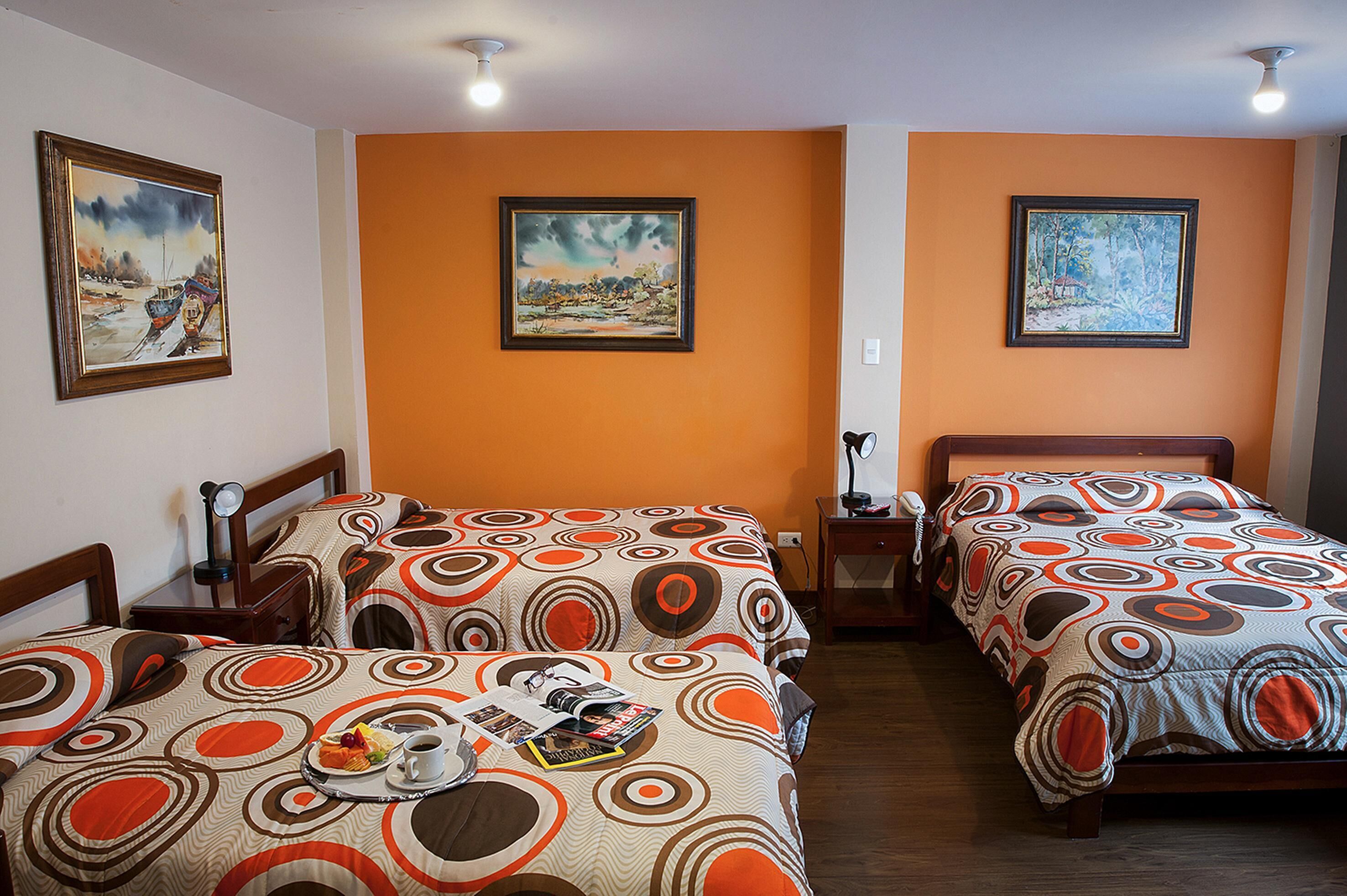 Une chambre d’hôtel avec deux lits, chacun recouvert d’une couvre-lit à motifs, une table de chevet avec une lampe et un tableau encadré au mur.