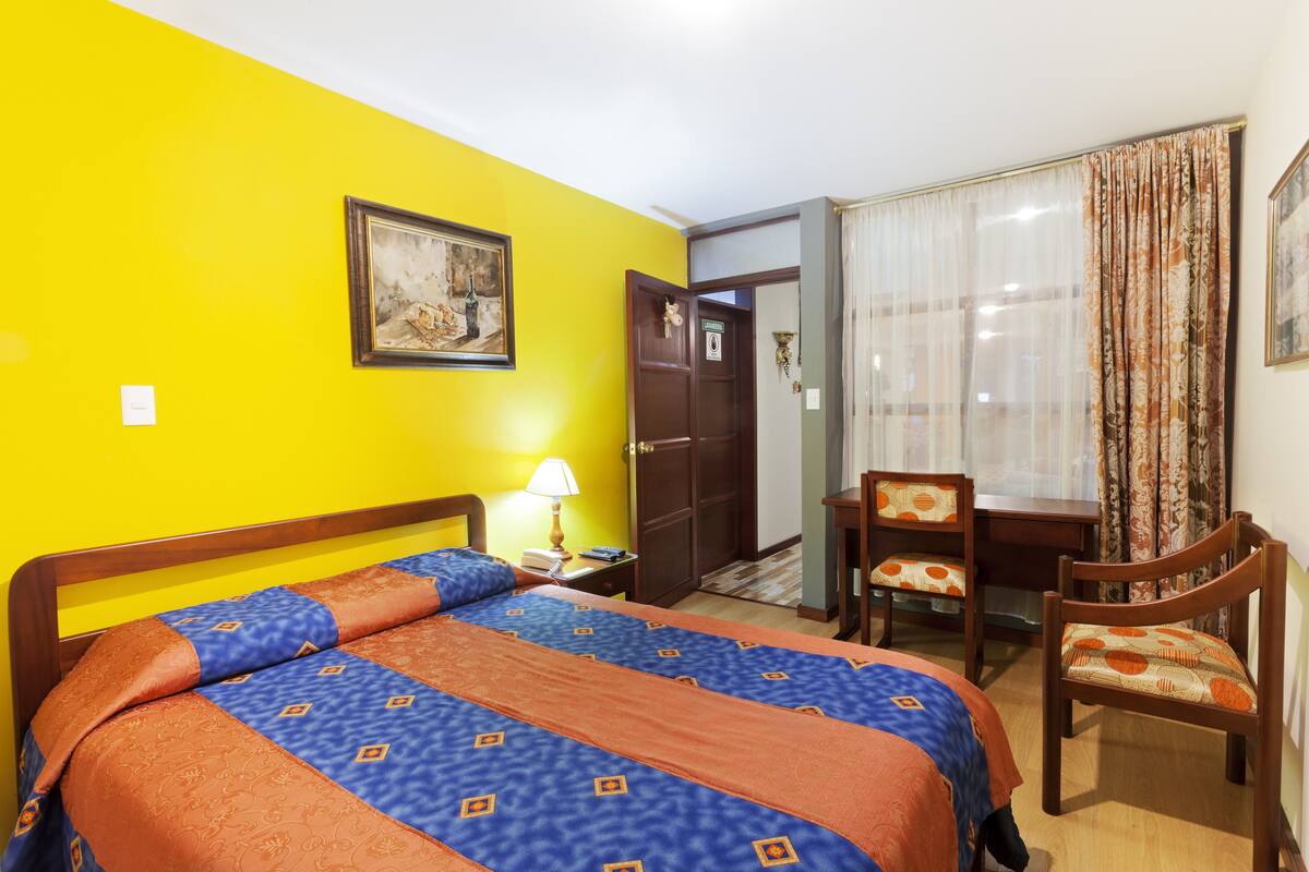 Een hotelkamer met een bed, een bureau, een stoel, een deur en een raam met gordijnen.