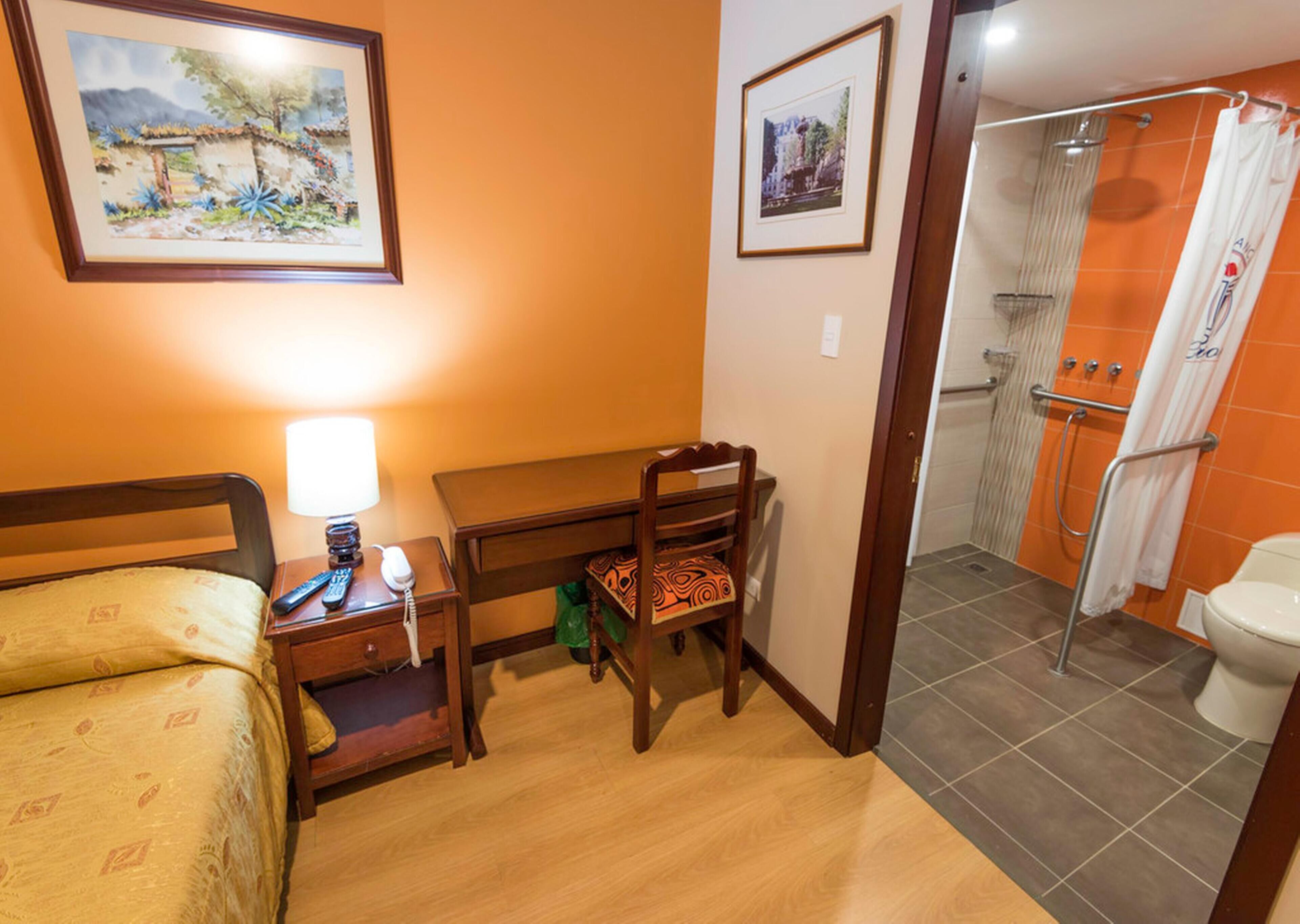 A hotel room with a bed, desk, chair, and a shower area.