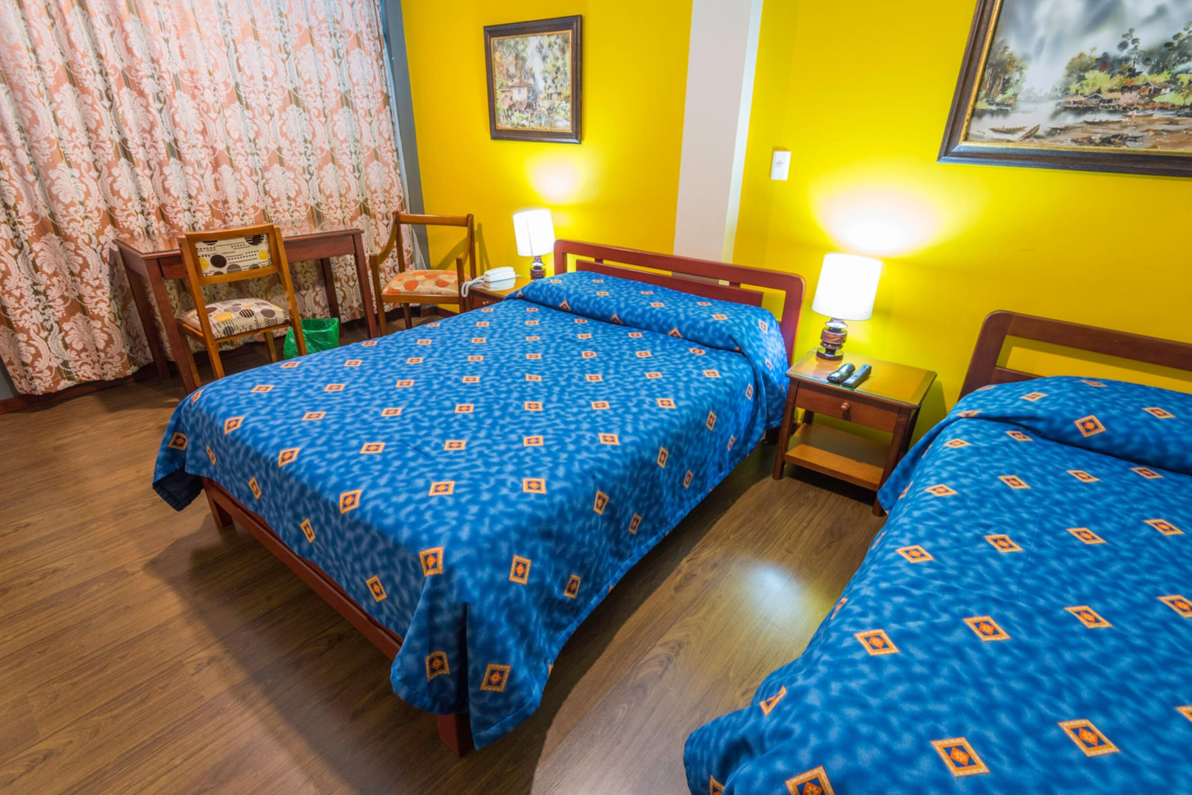 A hotel room with two beds, wooden furniture, a desk with chairs, and a curtain.