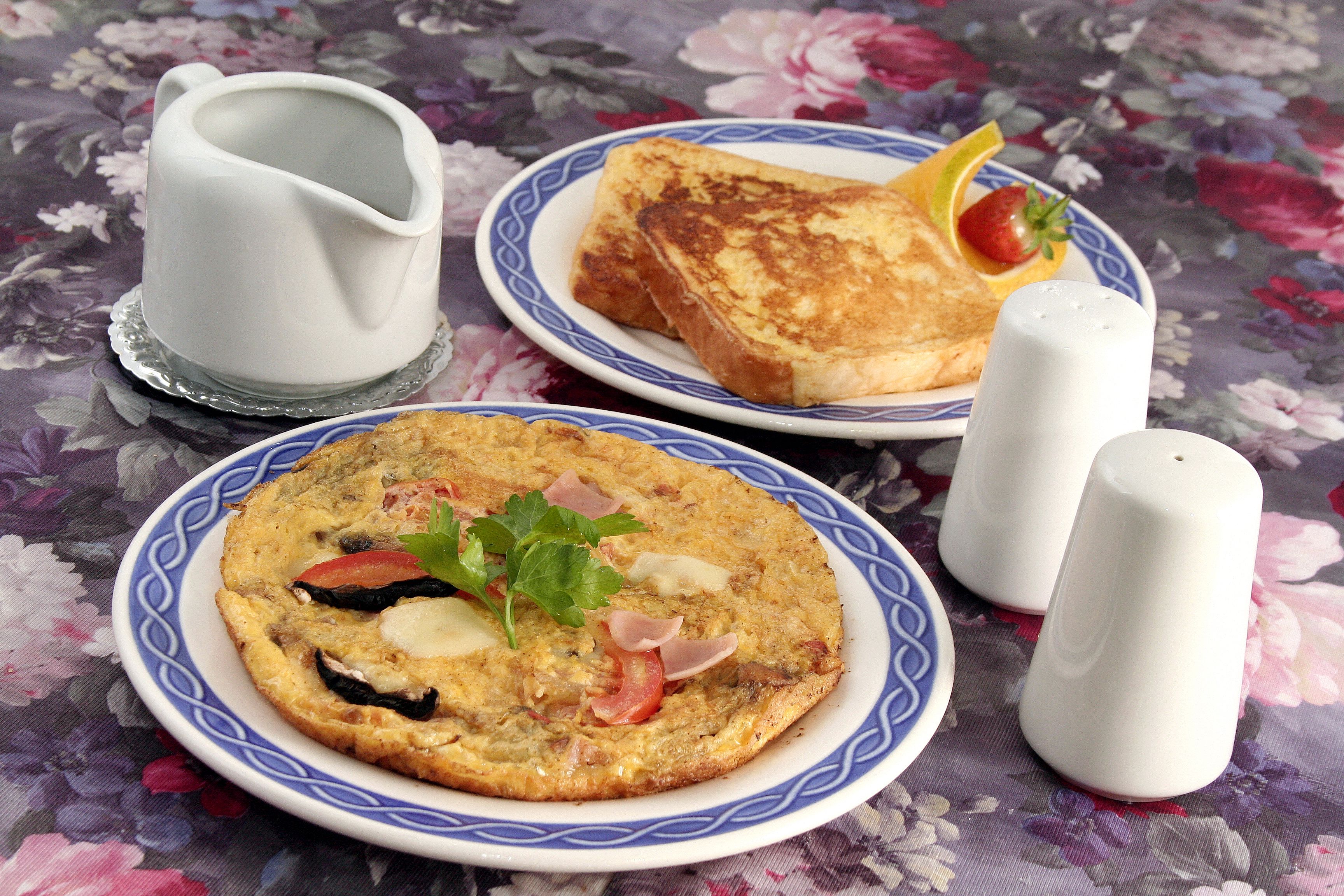 Two plates of food, one with toast and the other with an omelette, on a floral tablecloth.