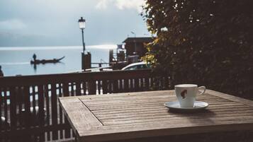 A wooden table with a white cup and saucer, overlooking a body of water with a boat and a distant shoreline.