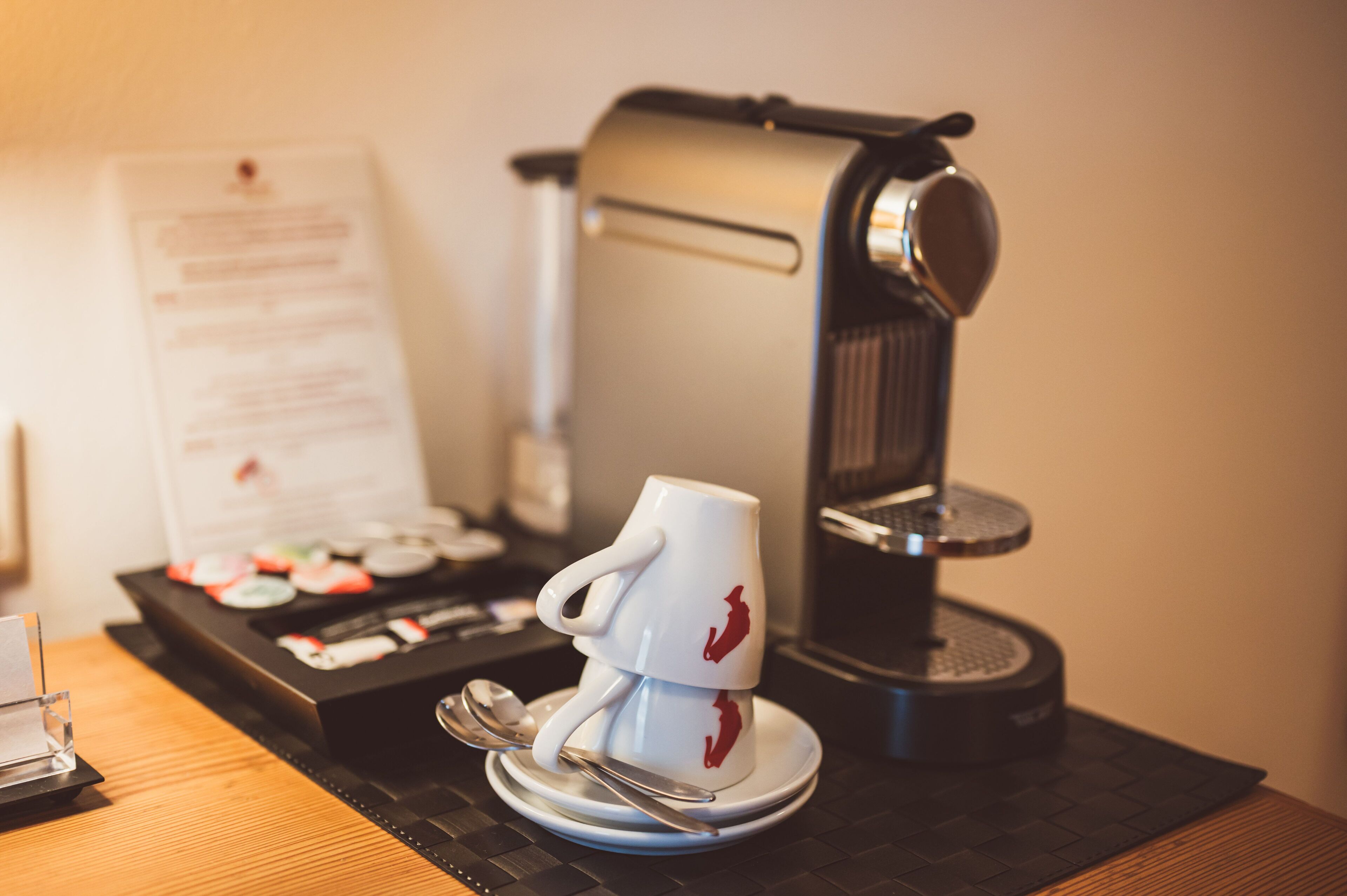 A coffee machine, a white mug with a red design, and a menu on a wooden table.