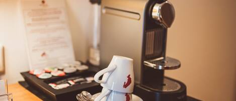 A coffee machine, a white mug with a red design, and a menu on a wooden table.