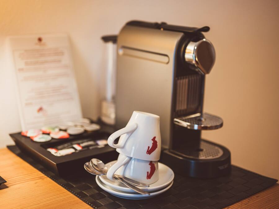 A coffee machine, a white mug with a red design, and a menu on a wooden table.