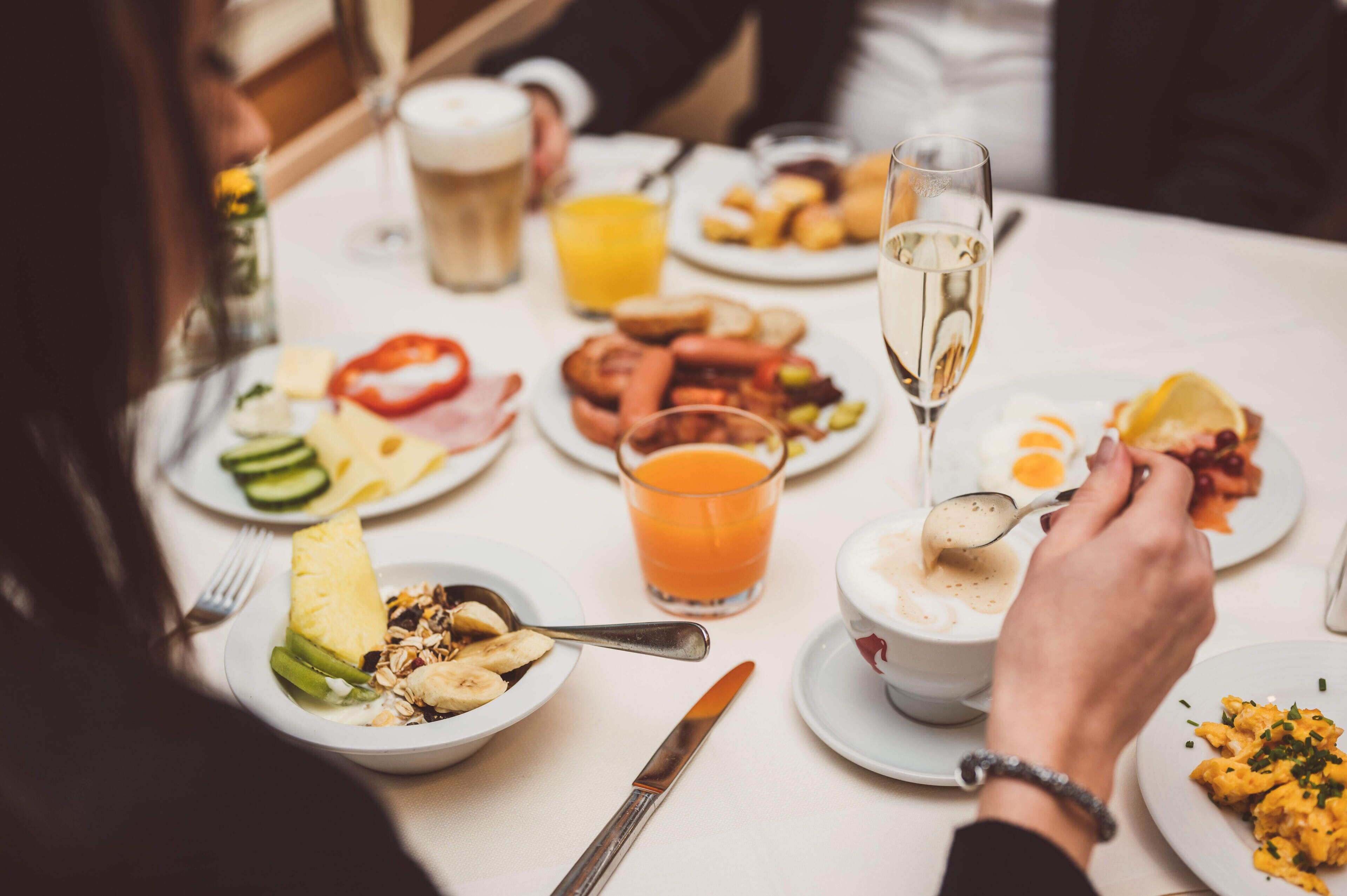 A breakfast table with various dishes, a glass of orange juice, and a glass of white wine.