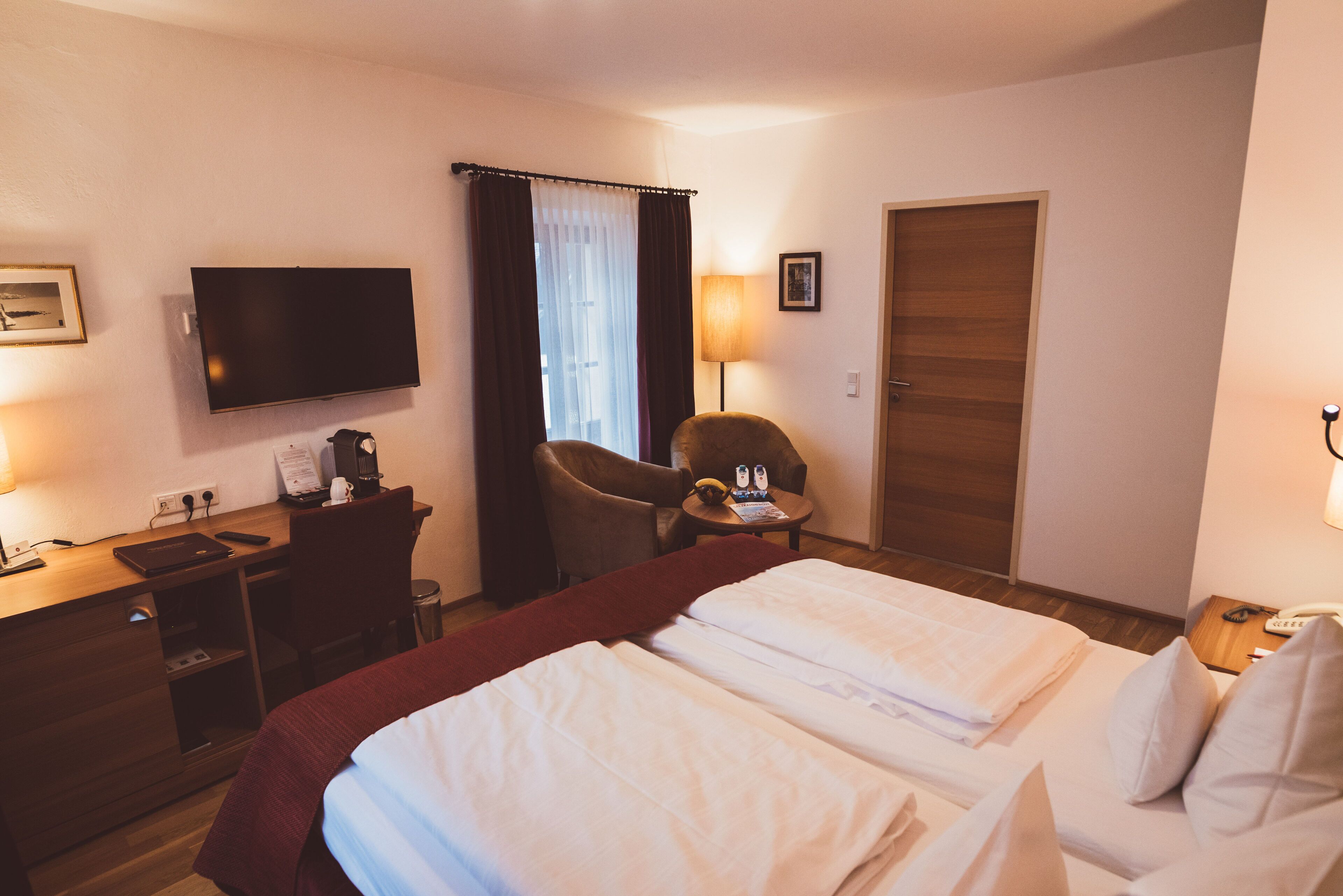 Habitación de hotel con dos camas, un escritorio, una silla, un televisor y una puerta.