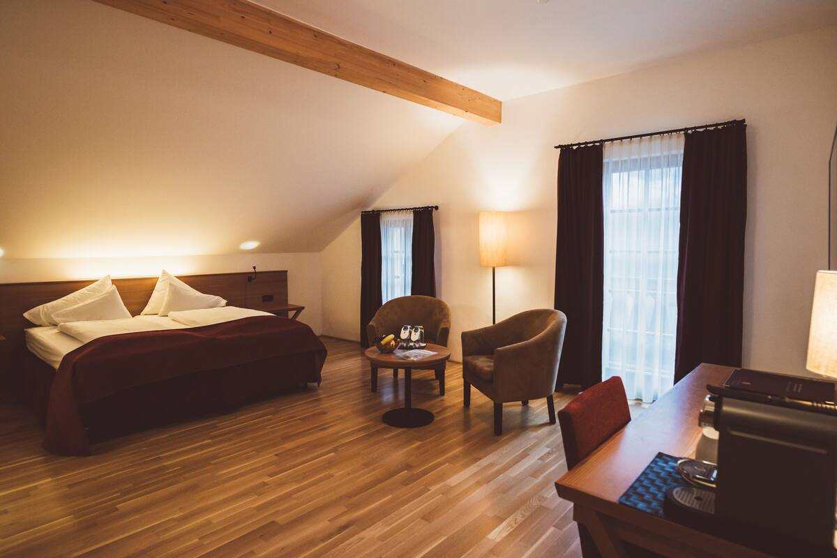 Ein Hotelzimmer mit Bett, Schreibtisch, Stuhl, Lampe und einem fensterbepflanzten Fenster.