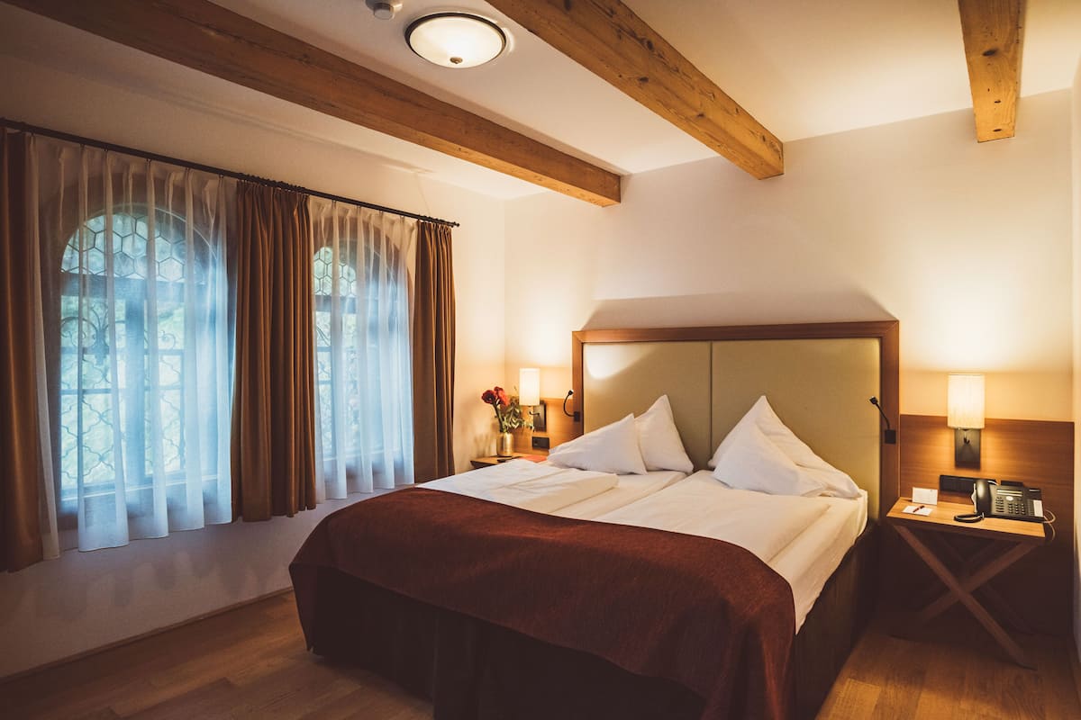 Ein Doppelbett mit Holz Kopfteil, ein Nachttisch mit Lampe und ein Fenster mit Vorhängen.