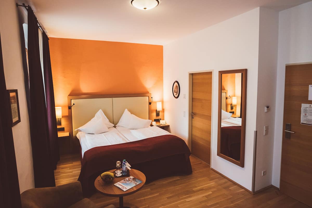 Ein Hotelzimmer mit einem großen Bett, Nachttischlampen, einem kleinen Tisch mit einer Zeitschrift und einem Spiegel an der Wand.
