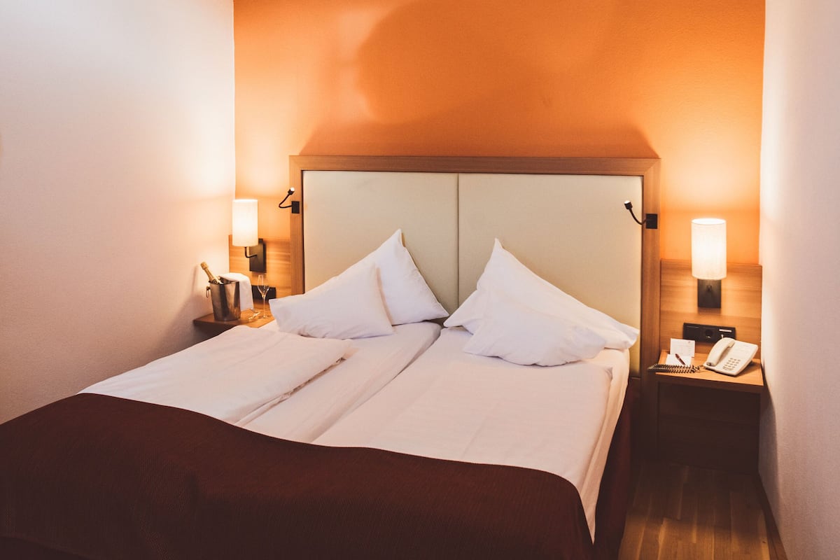 Ein Hotelzimmer mit einem großen Bett, zwei Nachttischen, einem kleinen Fenster und einer auffälligen Deckenleuchte.