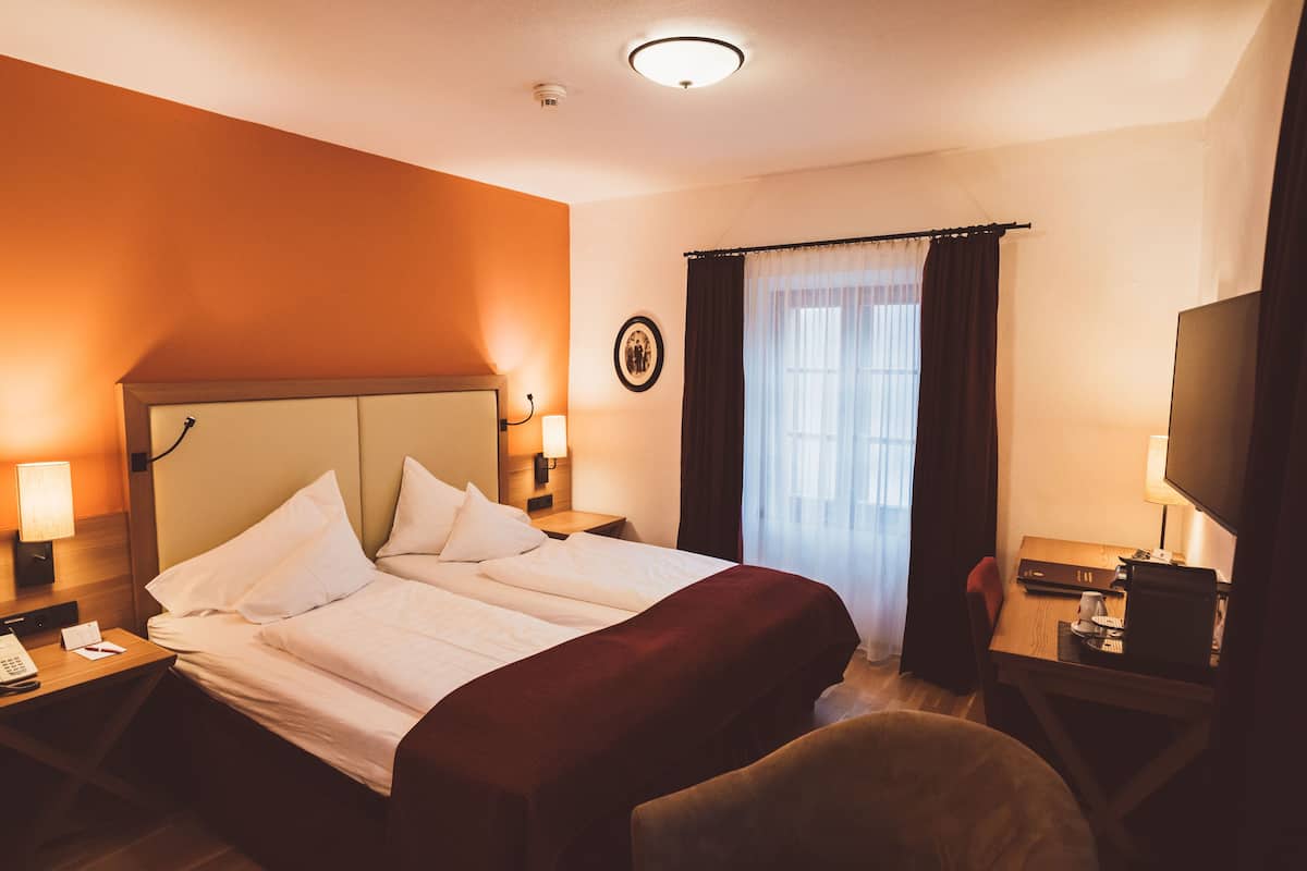 Ein Hotelzimmer mit einem großen Bett, Nachttischlampen, einem Schreibtisch und einem Flachbildfernseher sowie einem Fenster mit Vorhängen.