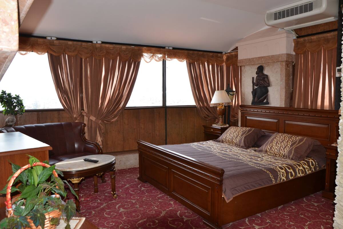 A hotel room with a wooden bed, a desk, a chair, a small table, and a statue.