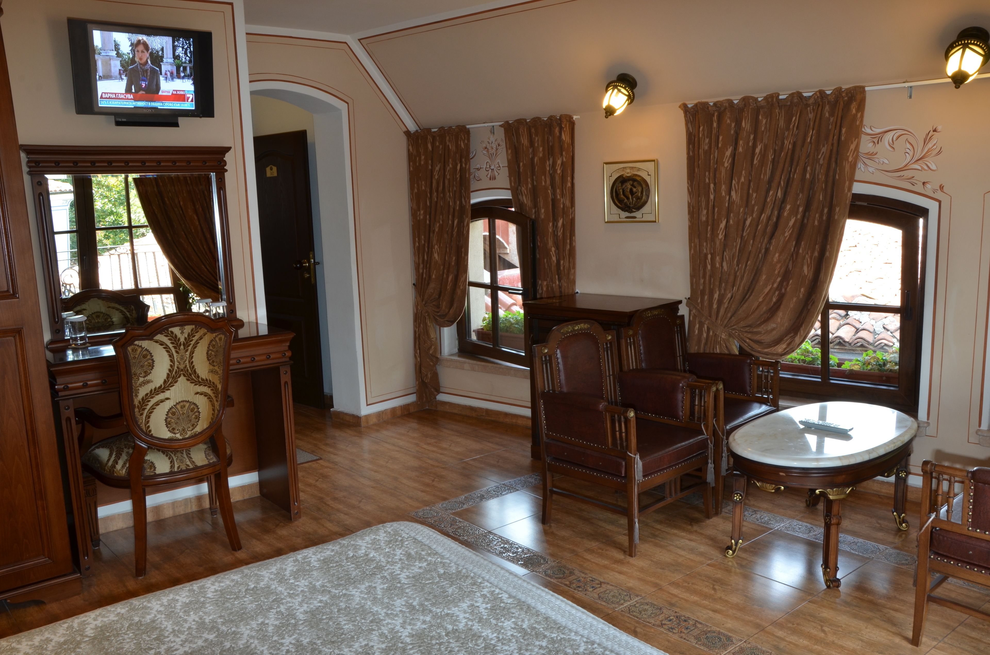 A room with a wooden dining table, two chairs, a sofa, and a television mounted on the wall.
