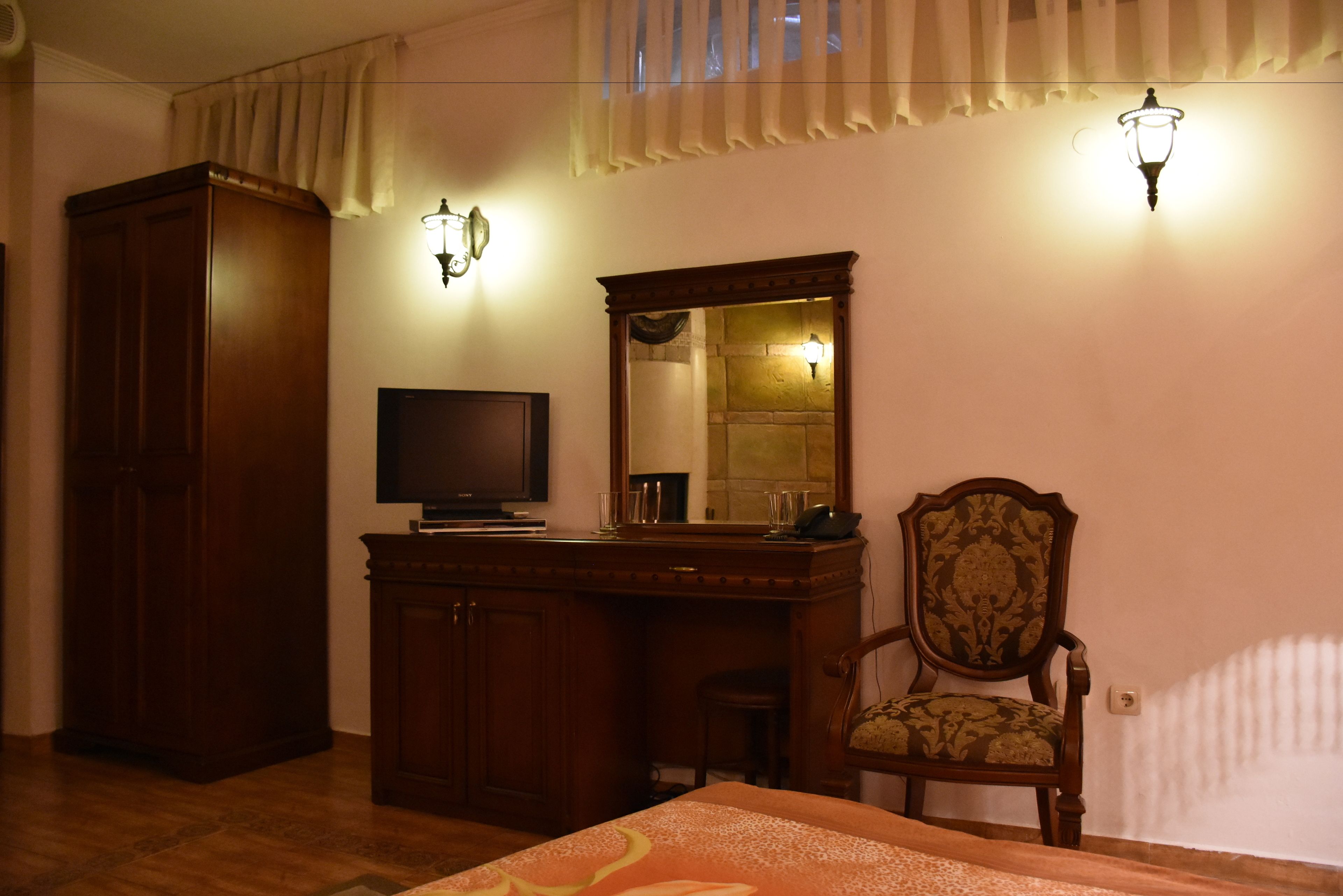 Une chambre à coucher avec une armoire en bois, un bureau avec un miroir, une télévision et une chaise.