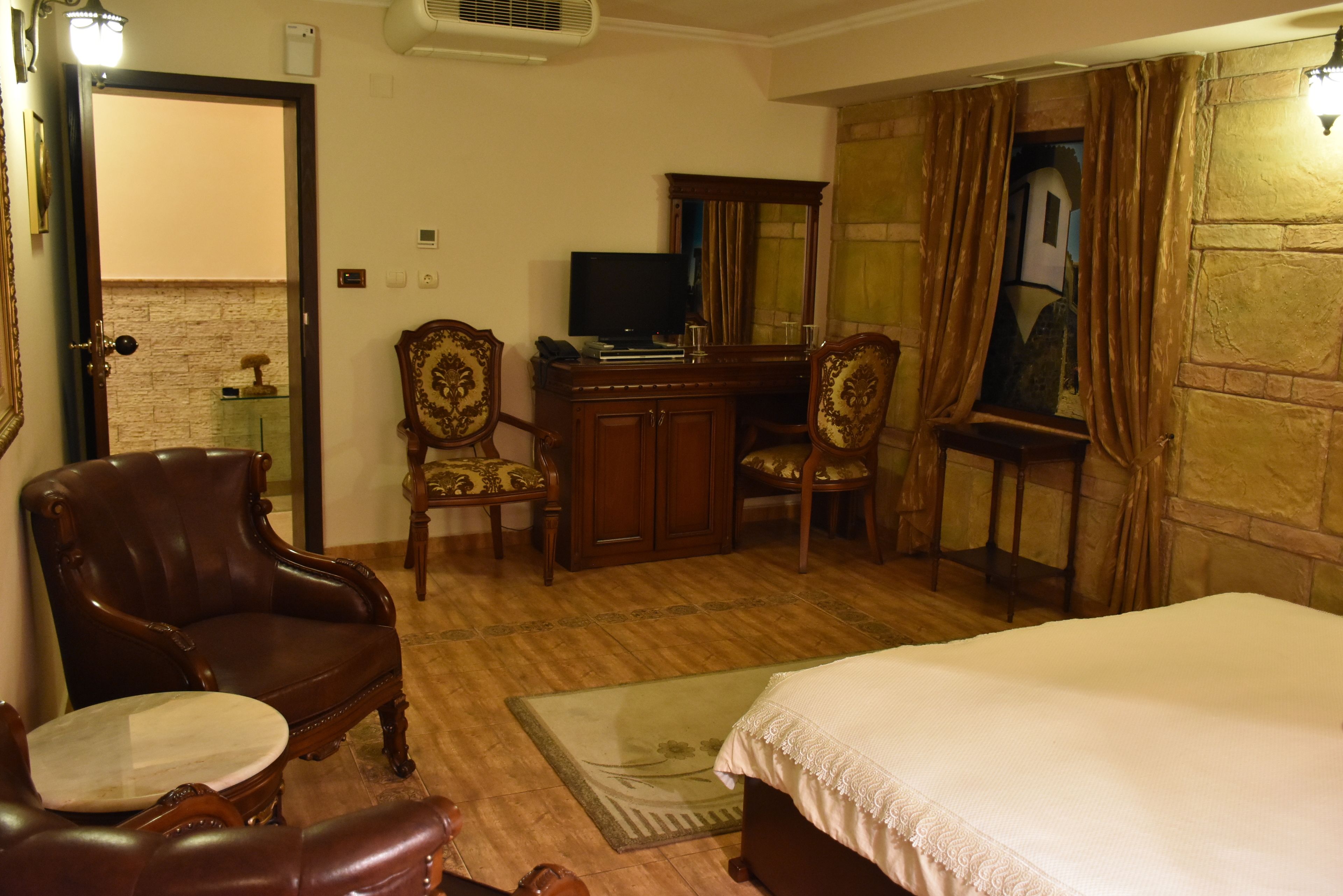 Een hotelkamer met een bed, een bureau met een computer, twee stoelen, een kleine tafel en een spiegel.