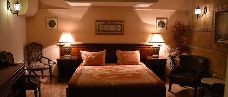 A hotel room with a large bed, two nightstands with lamps, a wooden dresser, a chair, and a potted plant.