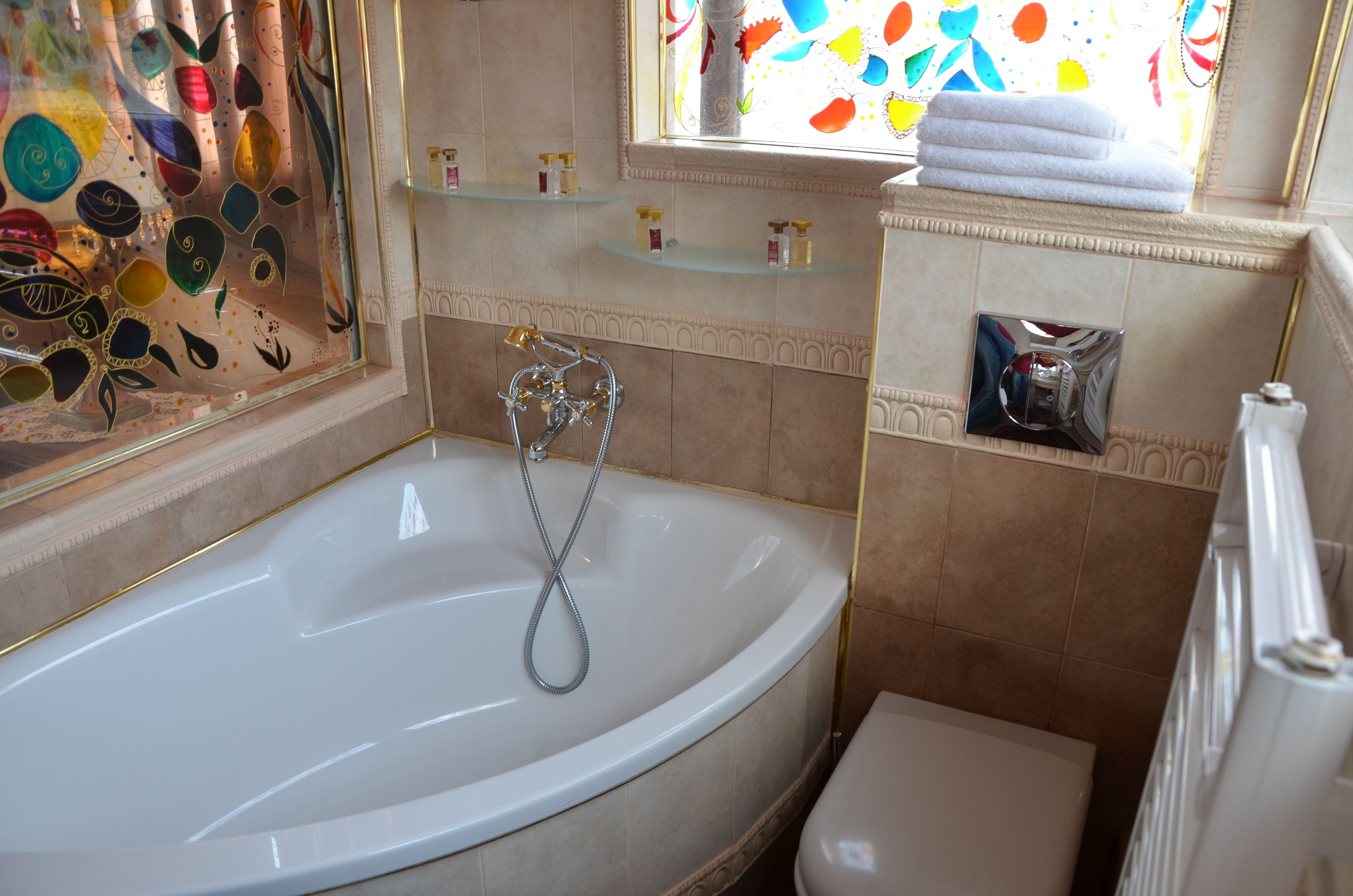 A bathroom with a freestanding bathtub, a toilet, and a window with colorful artwork.