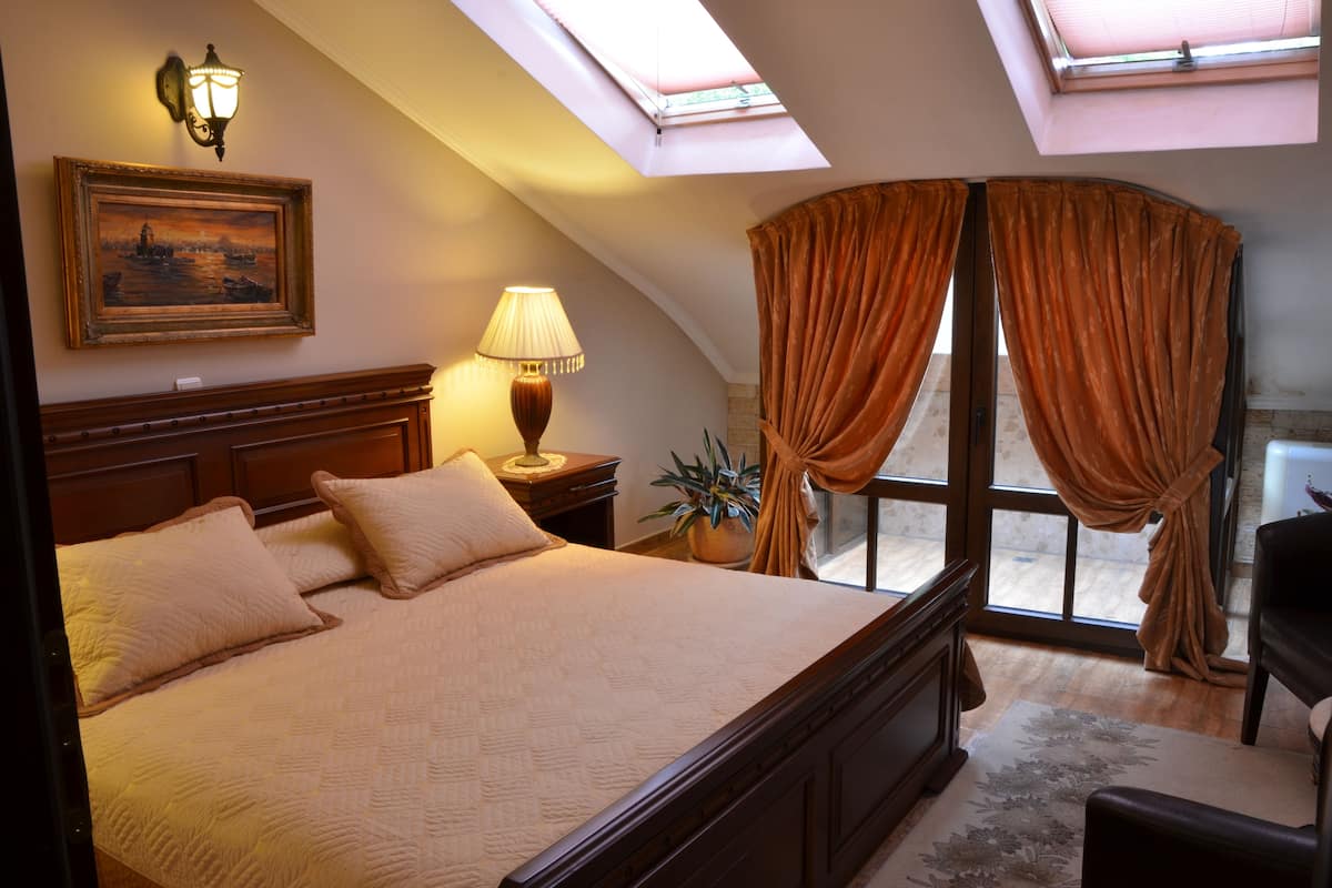 A bedroom with a large bed, a nightstand, a lamp, a framed picture, and a window with curtains.