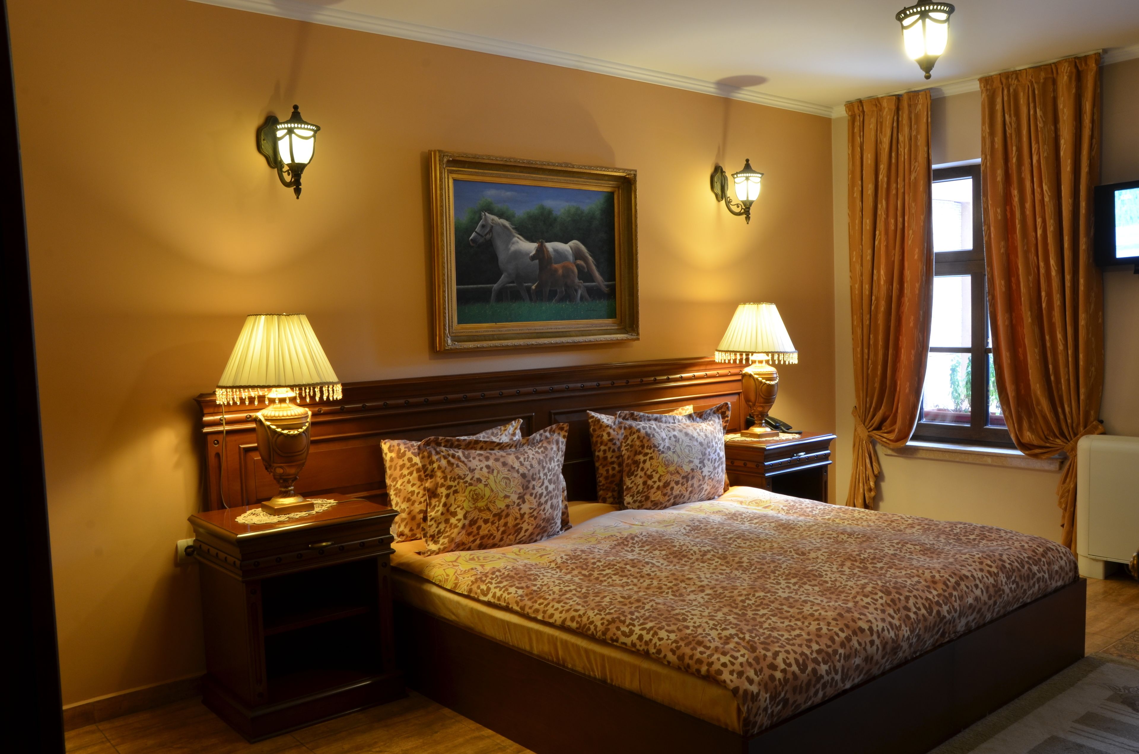 A hotel room with a large bed, two bedside lamps, a painting of horses, and a window with curtains.
