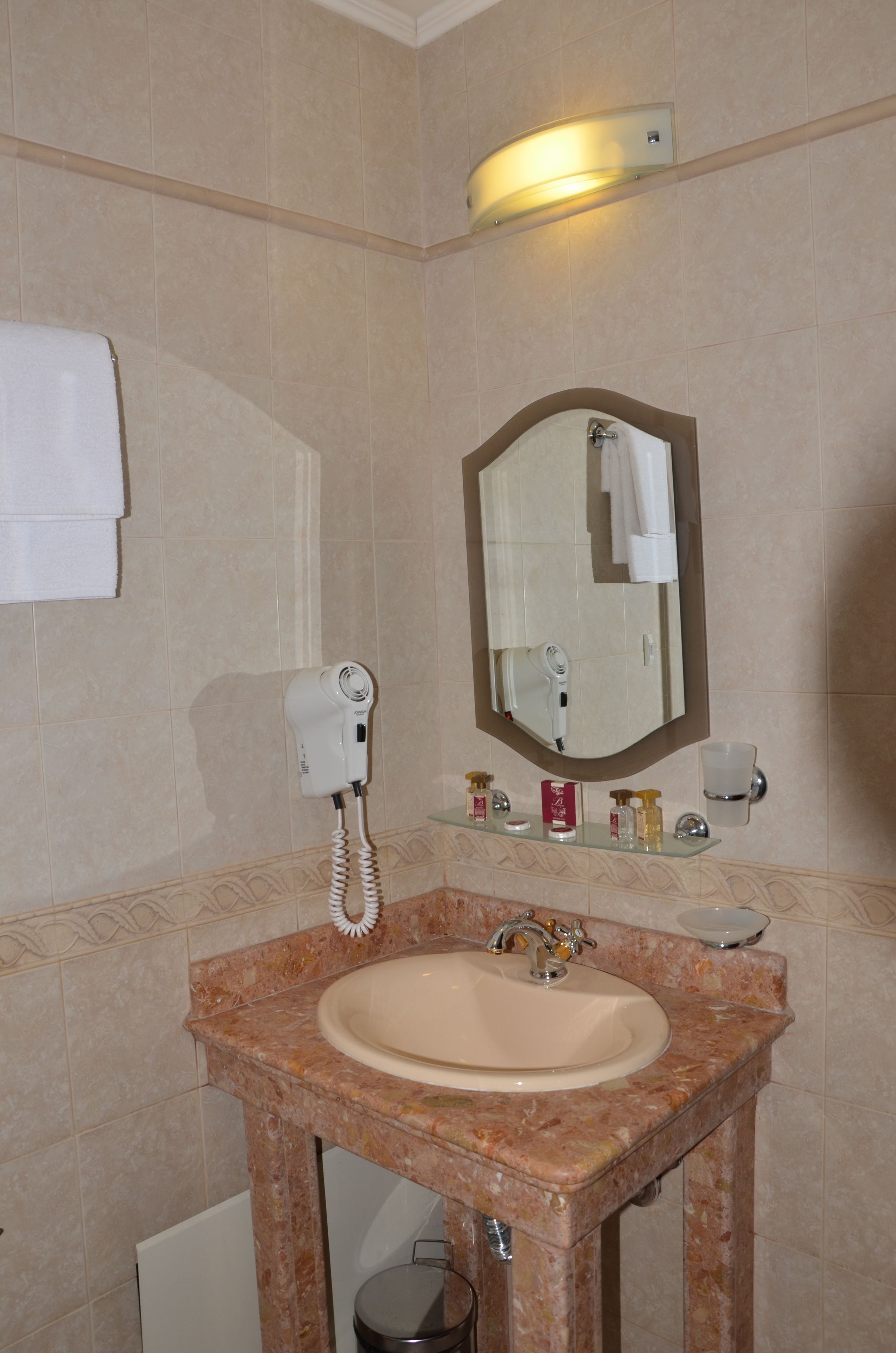 A bathroom with a marble sink, a hairdryer, a mirror, and toiletries on a shelf.