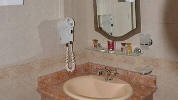 A bathroom with a marble sink, a hairdryer, a mirror, and toiletries on a shelf.