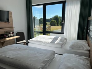 A hotel room with two beds, a desk with a television, and a window with a view of a grassy area.