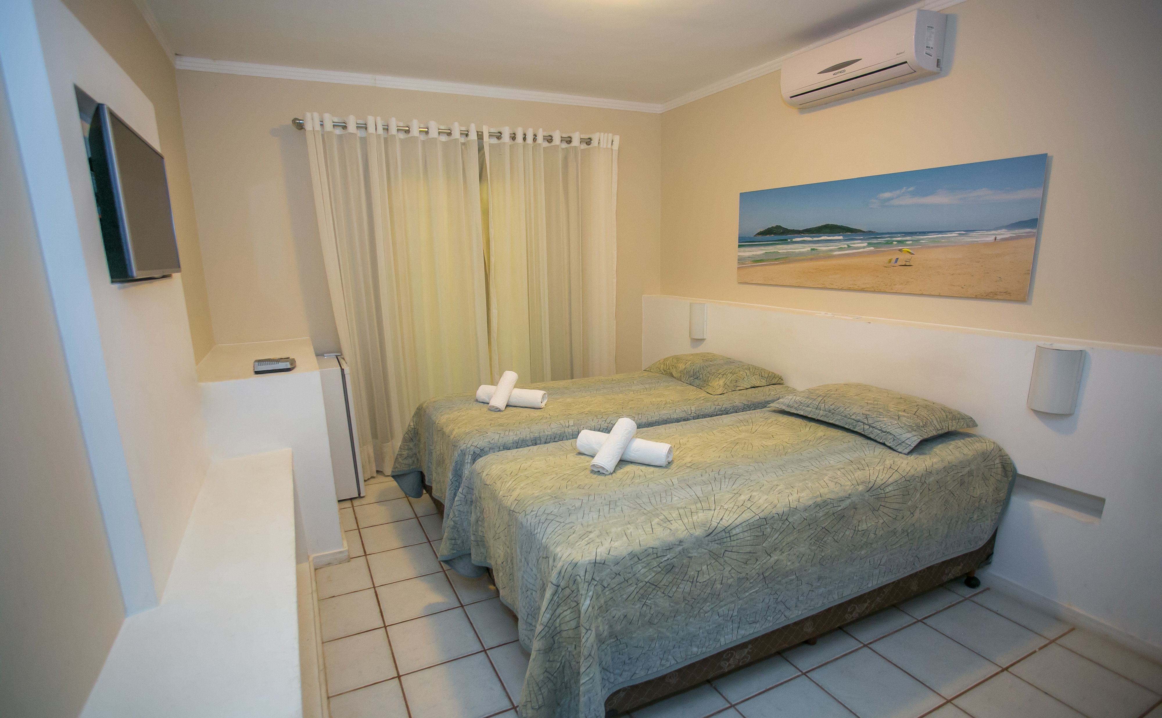 A hotel room with two beds, a painting of a beach, a curtain, and an air conditioning unit.