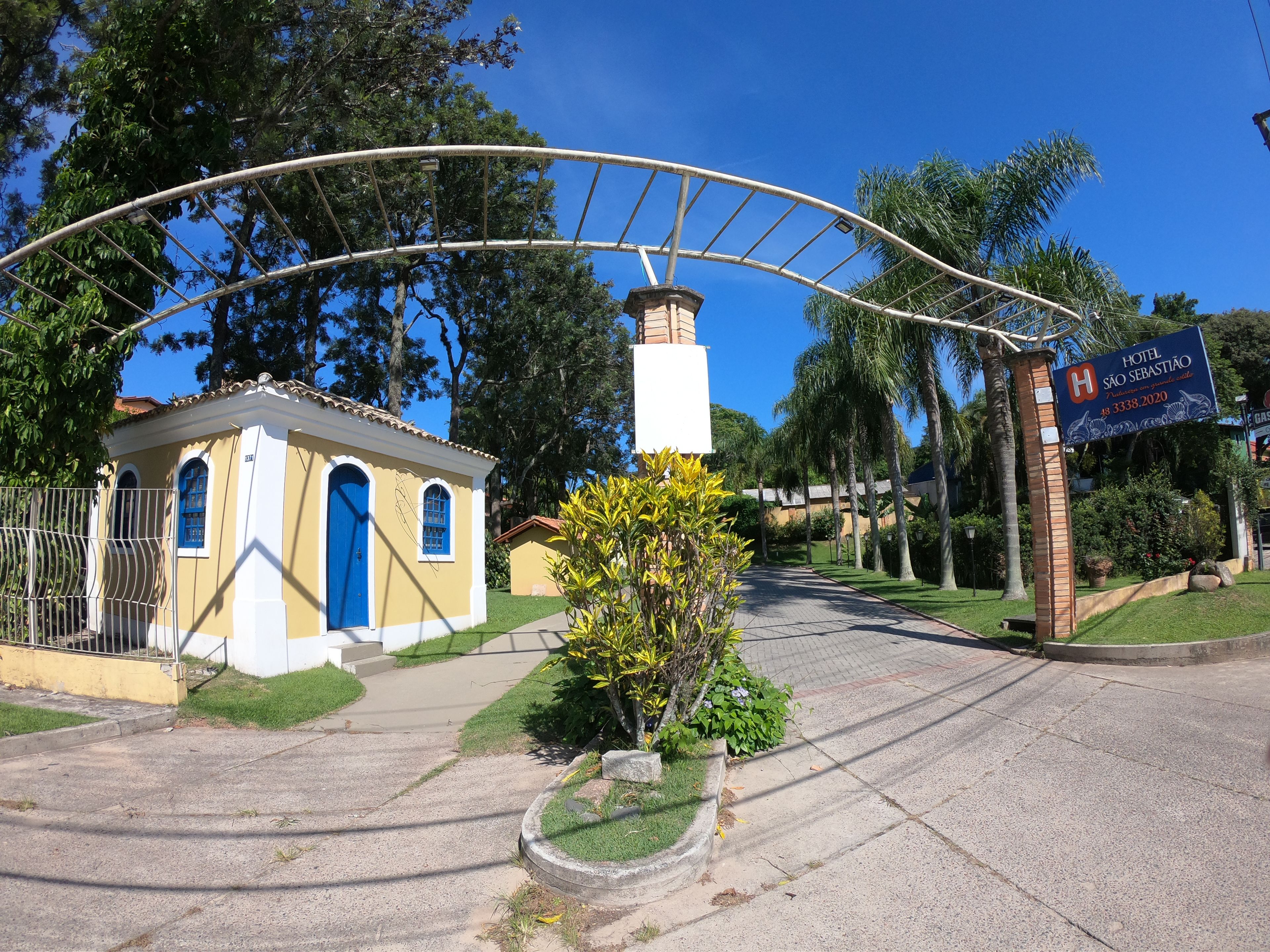 A hotel entrance with a sign for Hotel S ão Sebastião, a small building with a blue door, and a pathway leading to the hotel.
