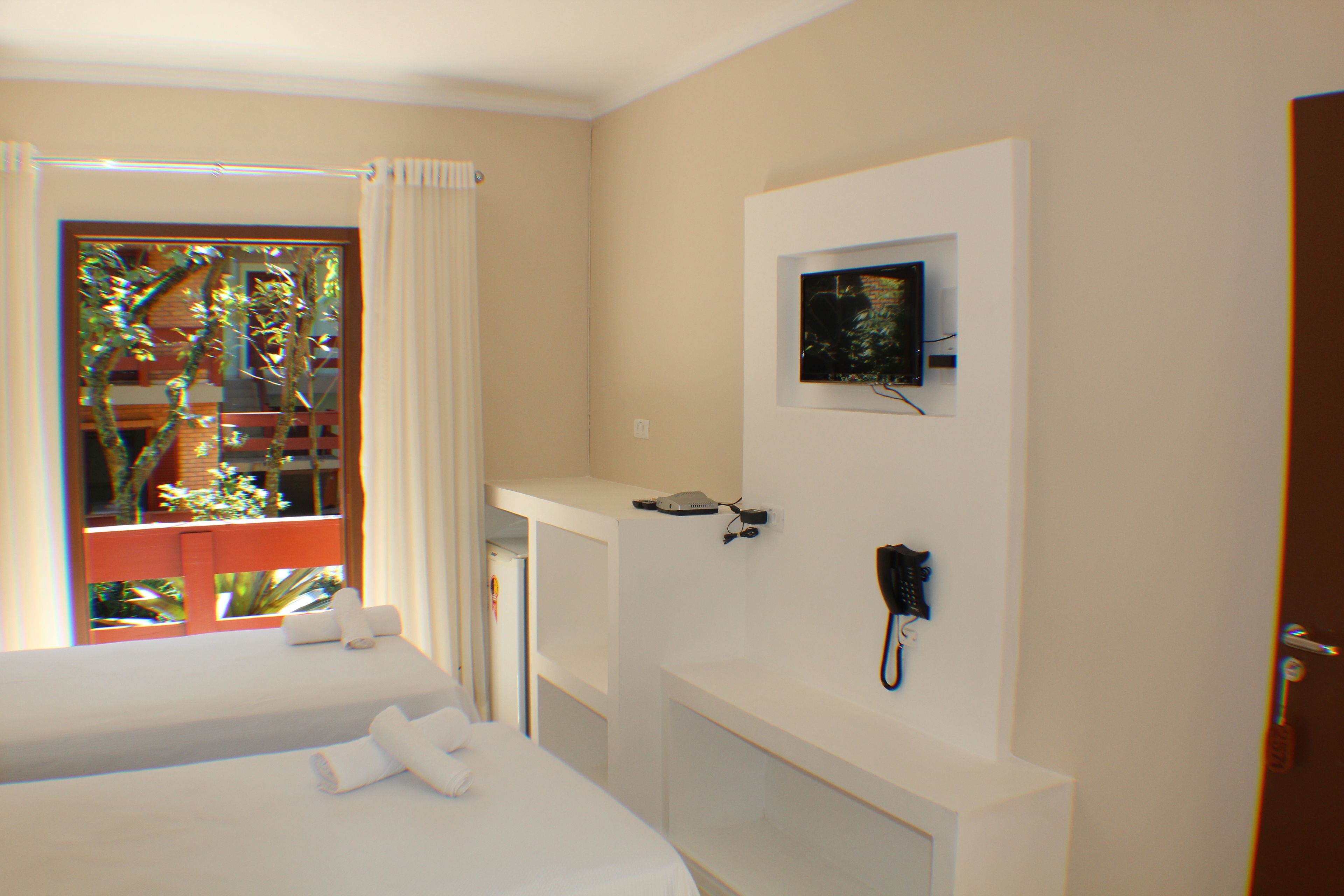 A hotel room with two beds, a window with curtains, a mounted telephone, and a small picture frame on the wall.